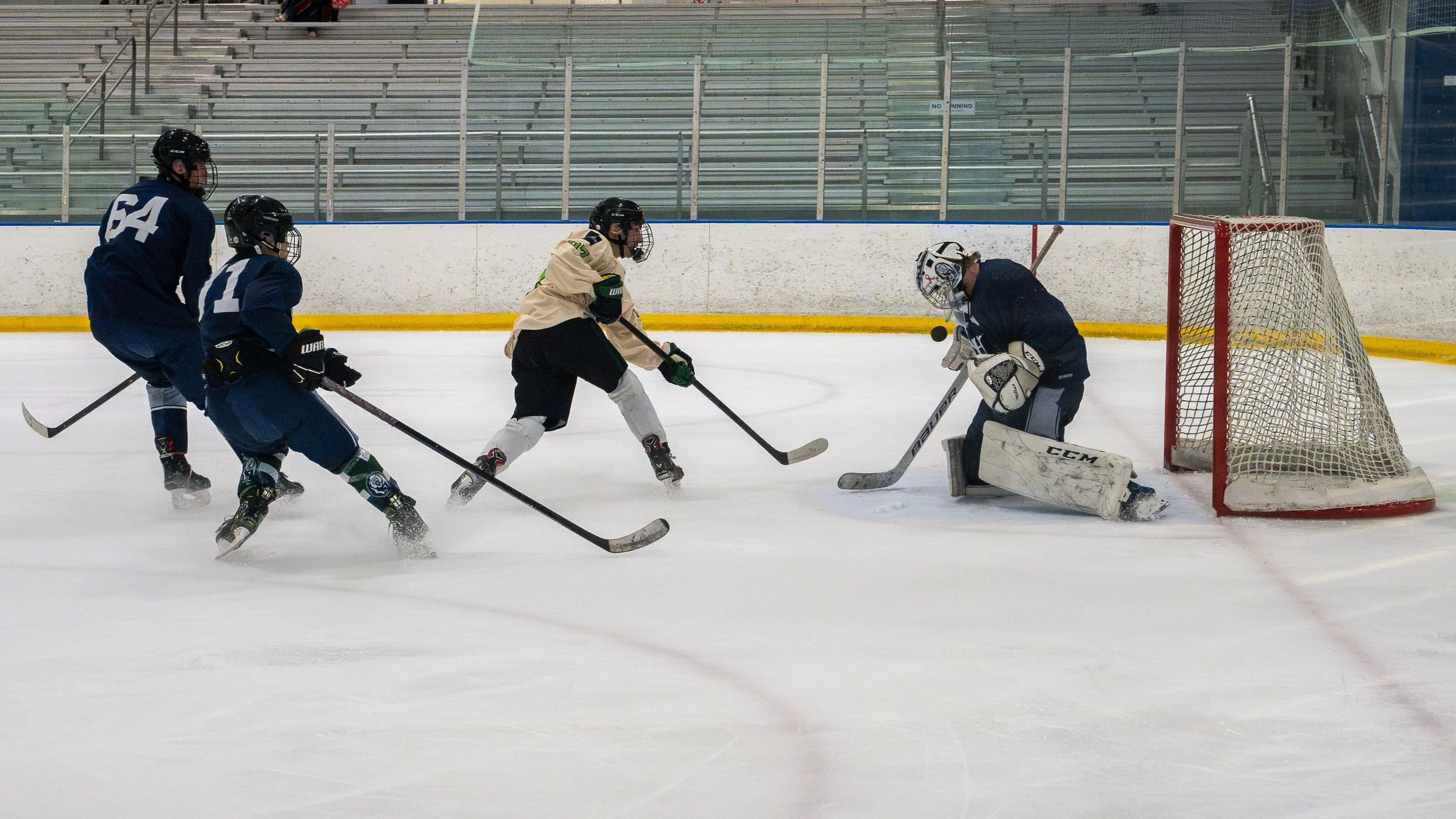 Hockey players and a goalie on the ice, with players attempting to score on the goal during a game.