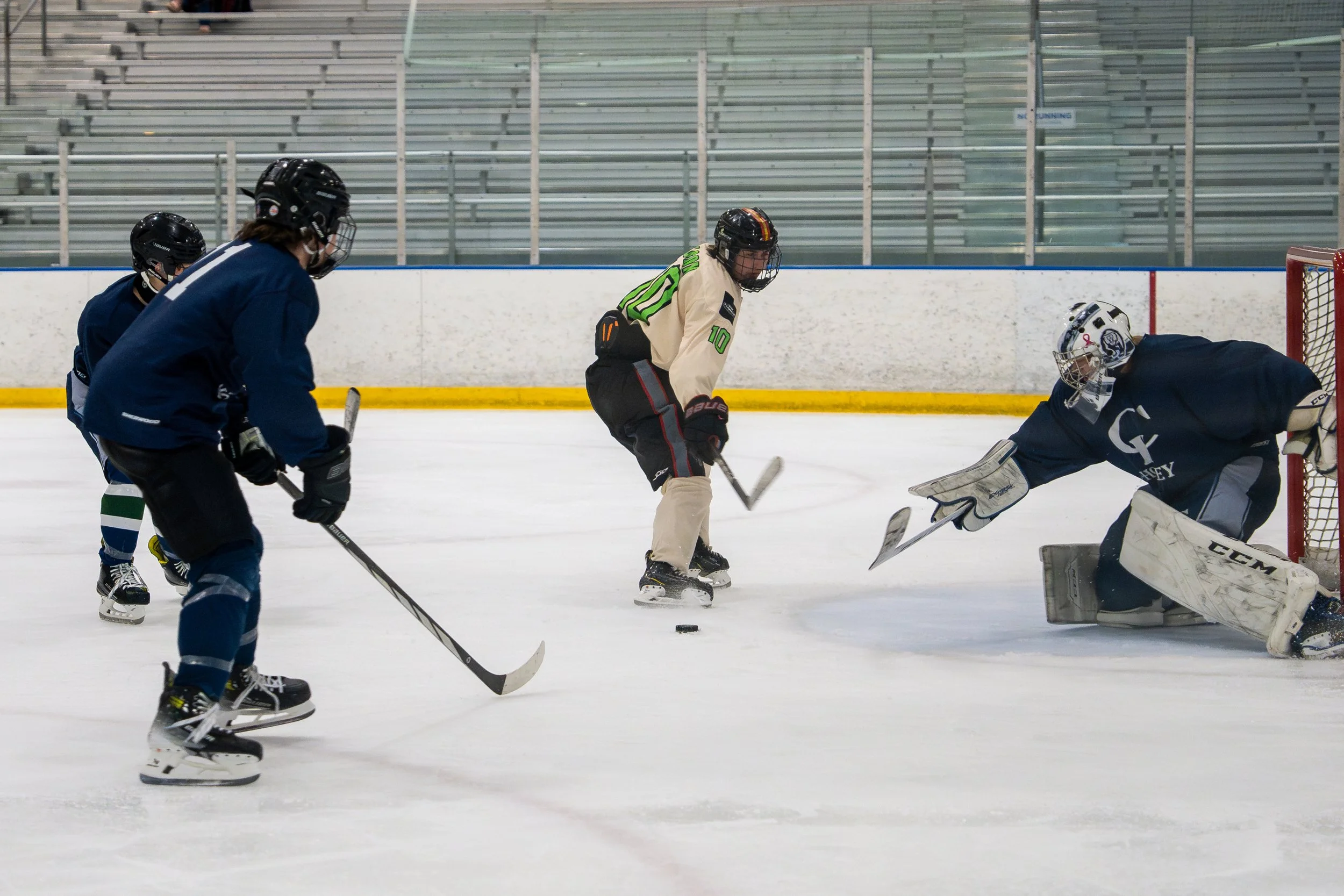 Hockey players on ice, with one goalie trying to block a shot, and other players in position near the goal.