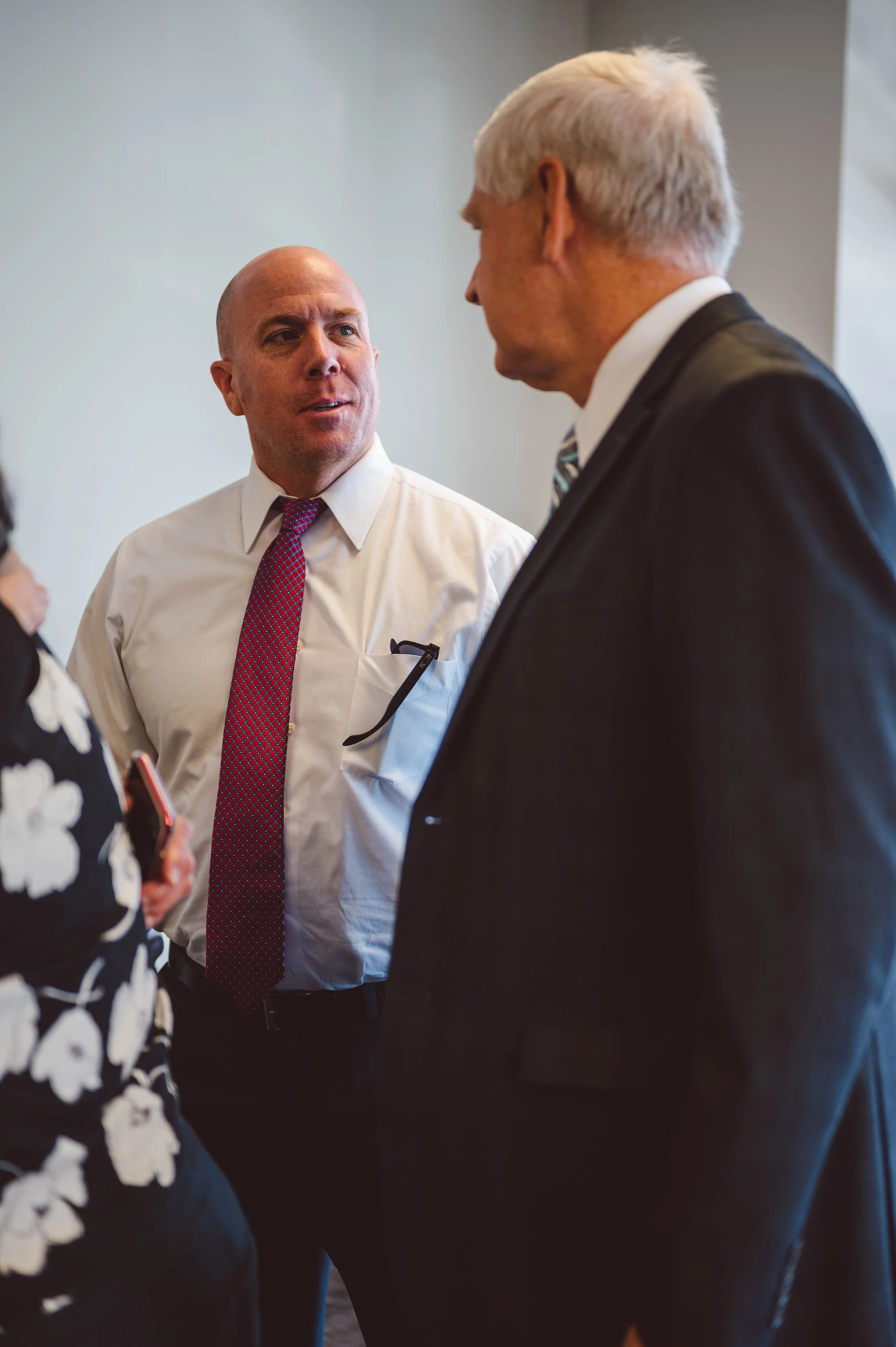 Three people having a conversation at a professional event, two men in suits and a woman in a floral blouse.