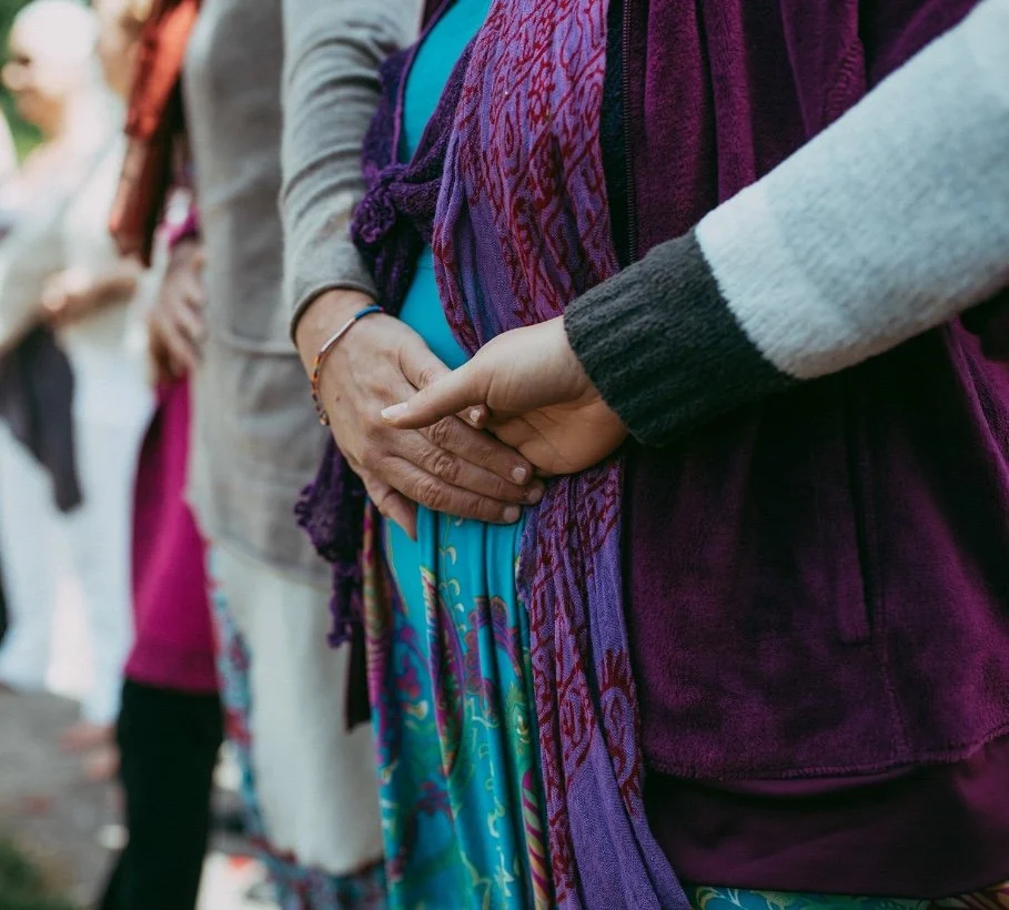 A group of woman standing outdoors, close up of holding hands over bellies.