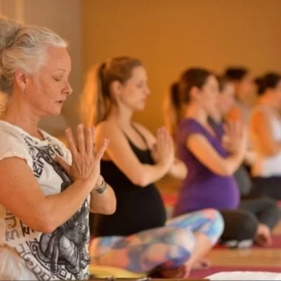 Marti sitting doing yoga with moms in the background