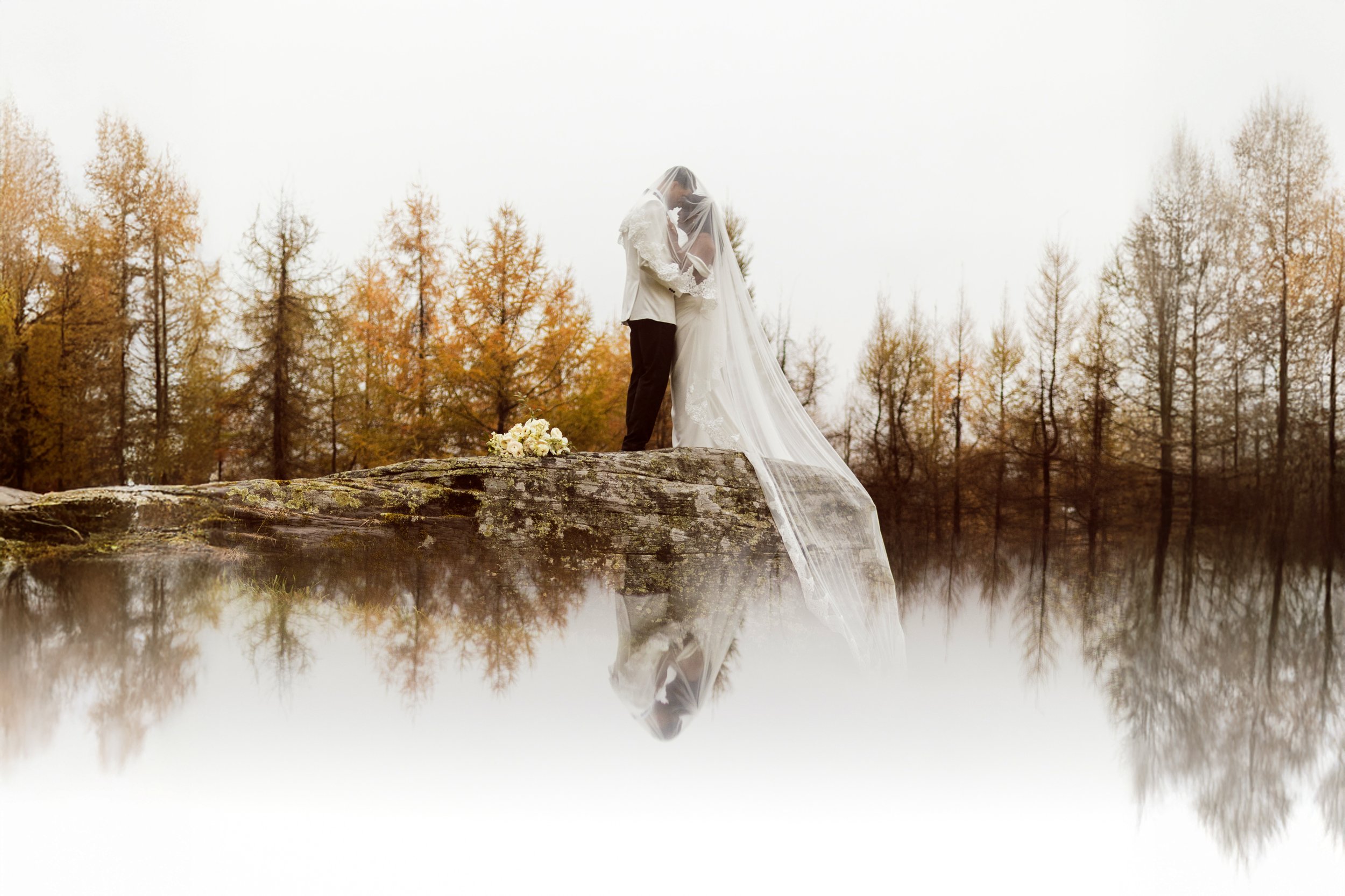 Intimate micro wedding at The Venue at Carley Brook in the Poconos, featuring a bride and groom embracing on a mossy rock with autumn reflections