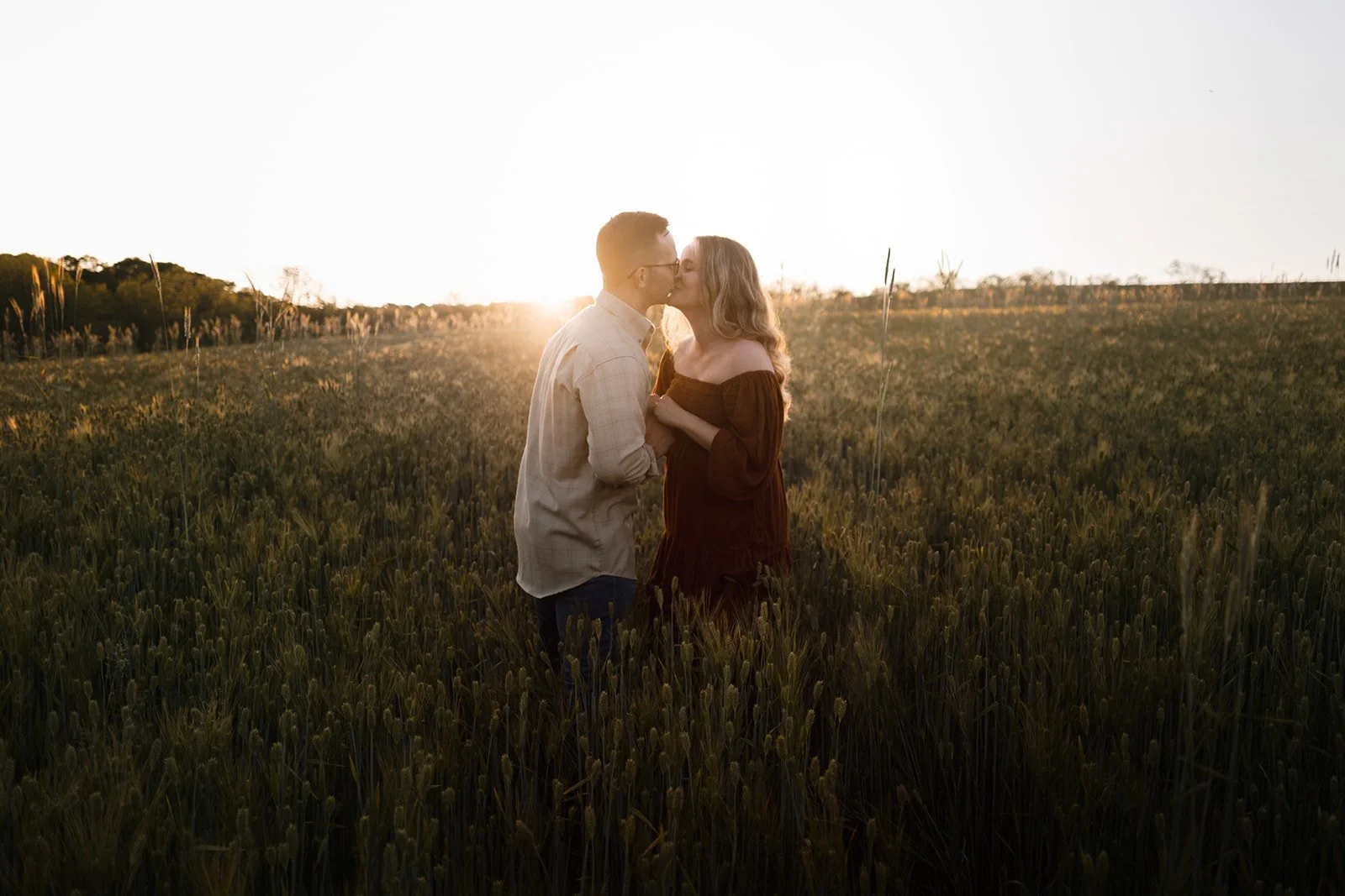 A couple sharing a kiss in a field at sunset.