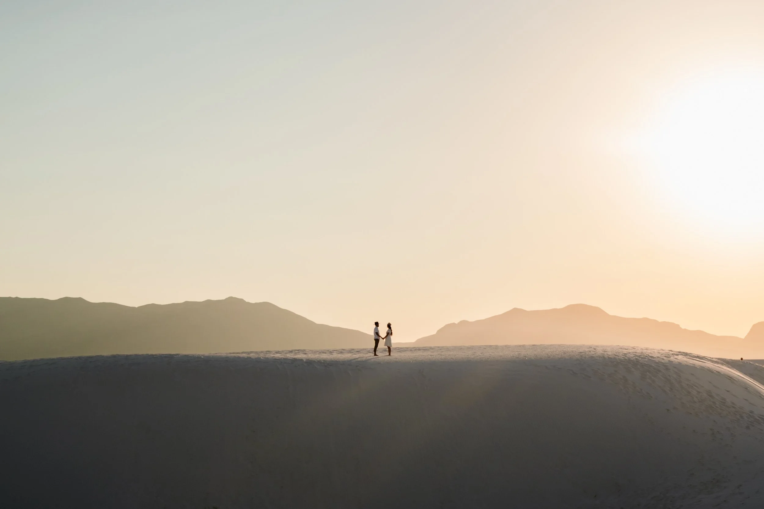 Minimalist elopement photography by a Lancaster, PA wedding photographer; couple holding hands on a vast white sand dune at sunset.