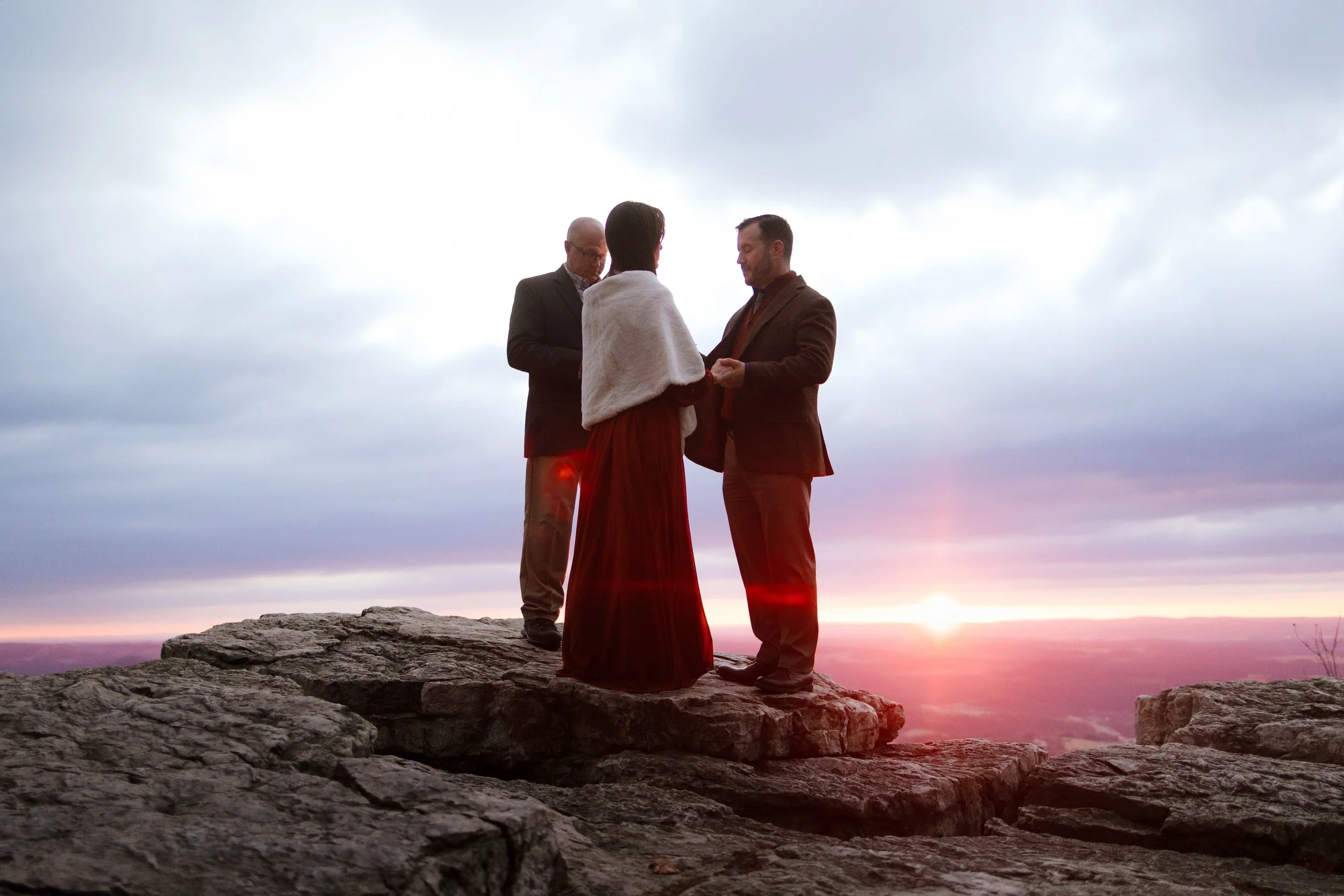 Candid shot of a couple eloping in the Poconos during winter, wrapped in a faux fur shawl with red sunrise in the background