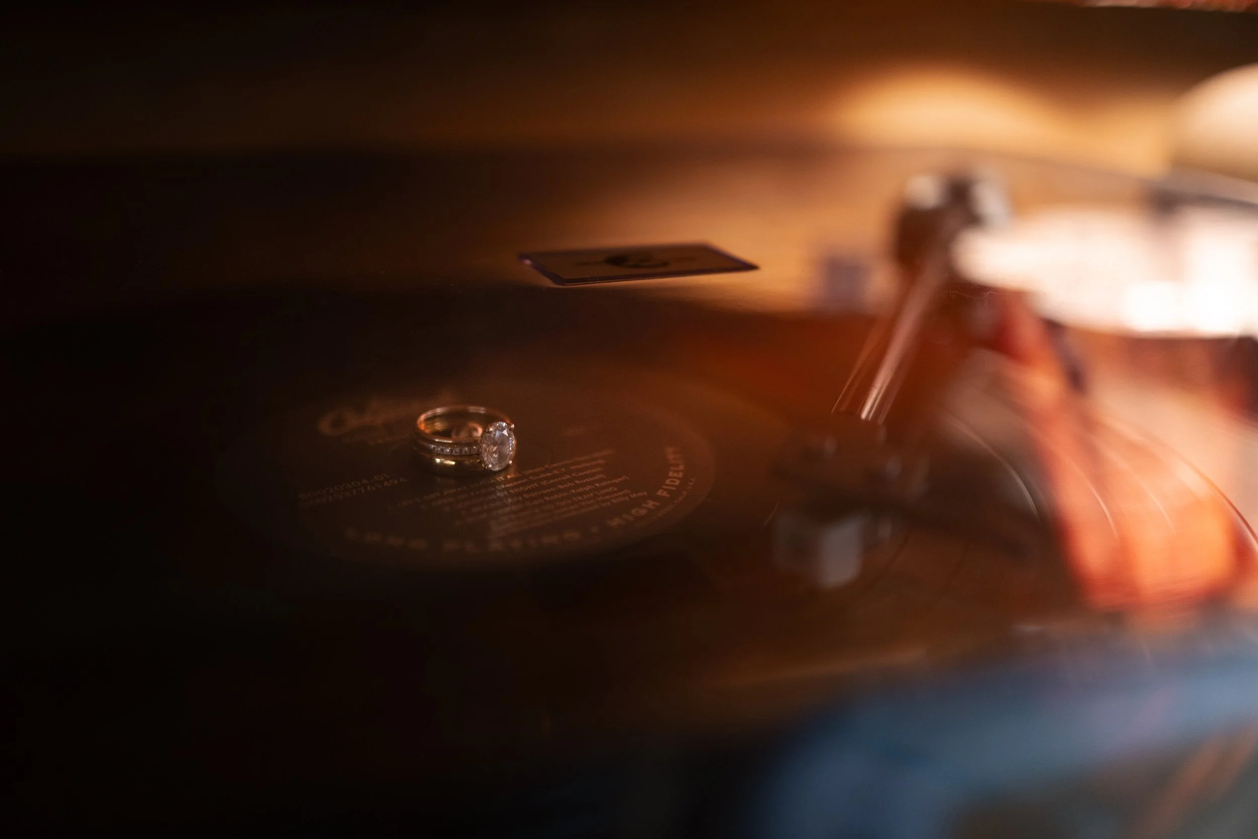 A close-up of a diamond ring placed on a vintage record player spinning a vinyl record.
