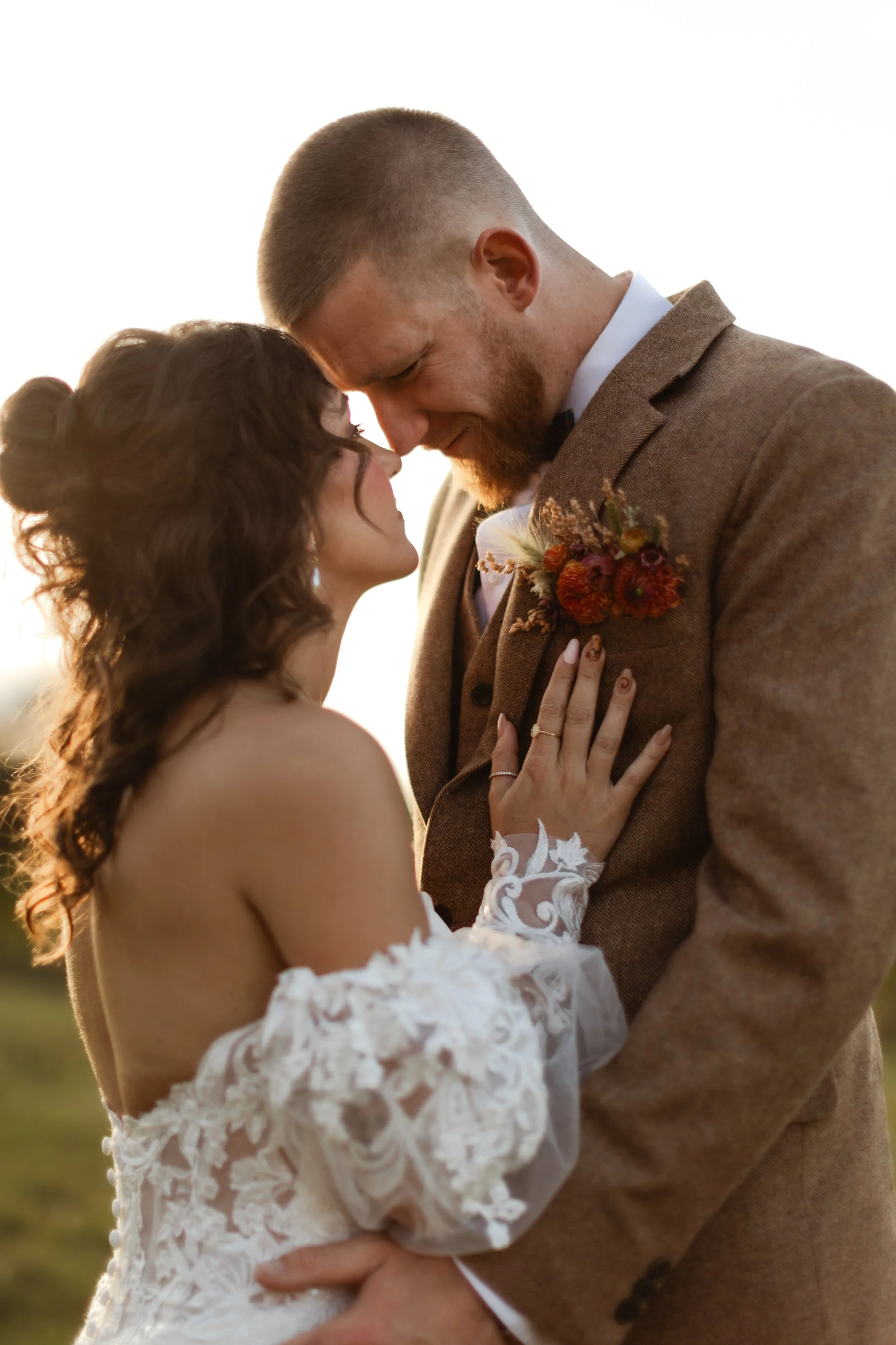 A couple in wedding attire sharing an intimate moment outdoors at sunset.