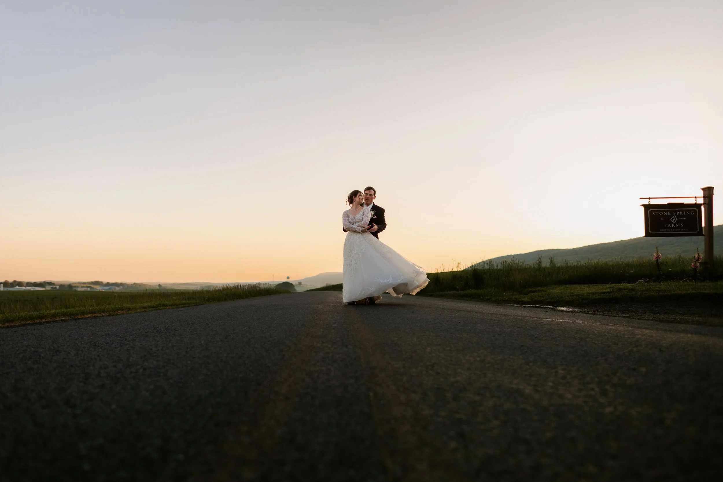 Golden hour wedding portrait of a bride and groom during sunset at Stone Spring Farms in Hamburg, PA. Wide landscape couple photography by a Berks County wedding photographer capturing the scenic countryside.