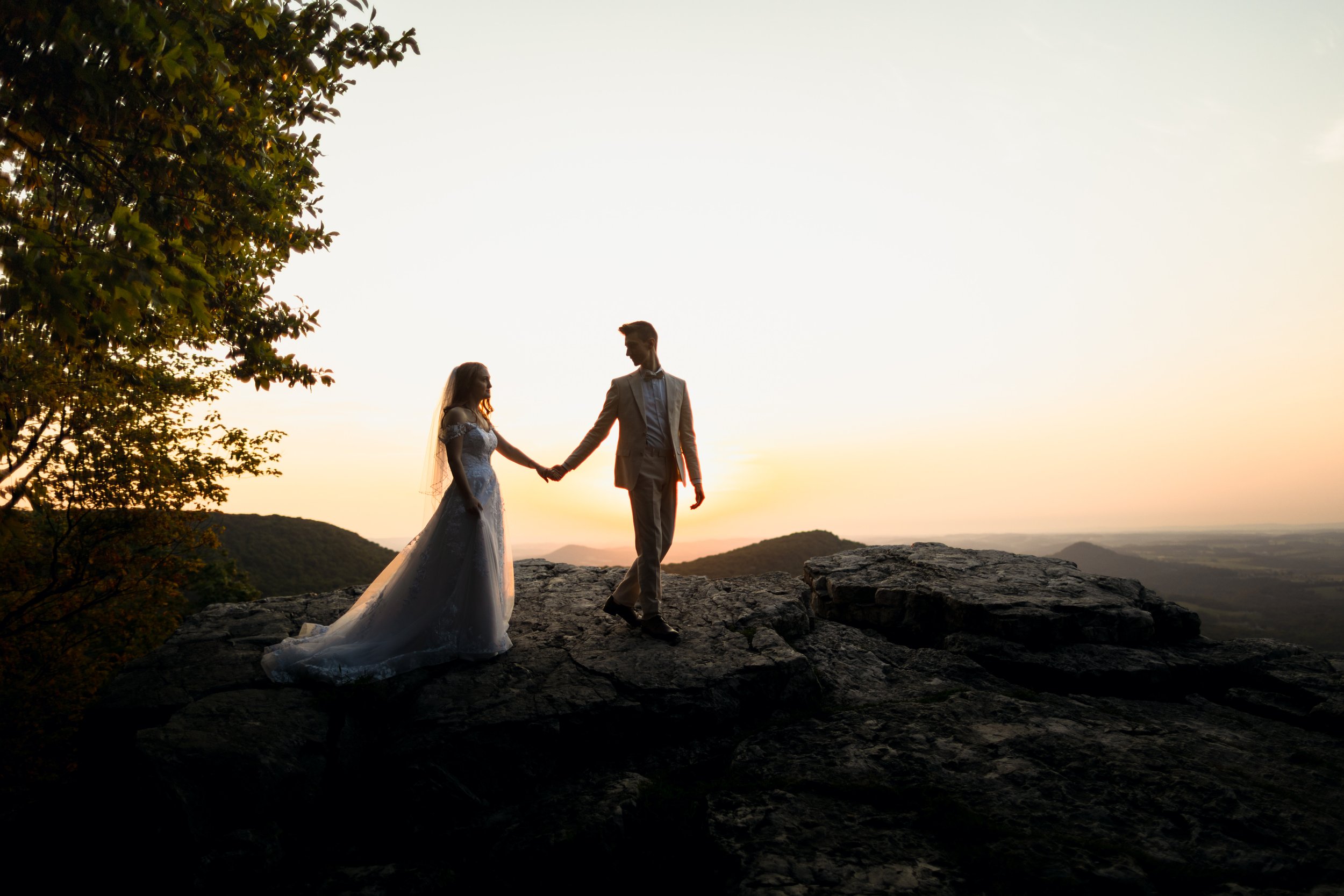 Bride and groom holding hands and walking along a rocky mountain ridge trail during a Pennsylvania sunrise elopement