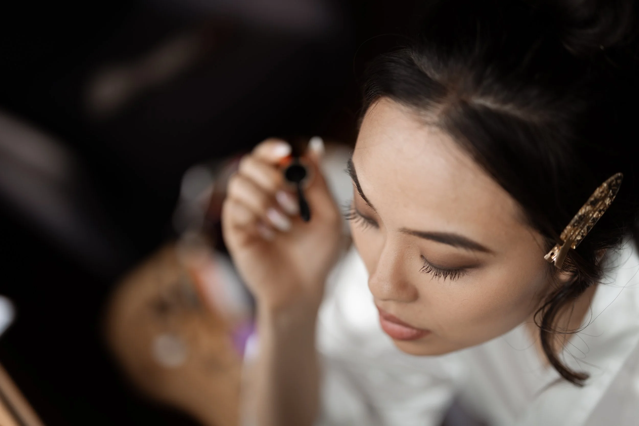 A woman with dark hair and a hair clip is applying makeup with a brush.