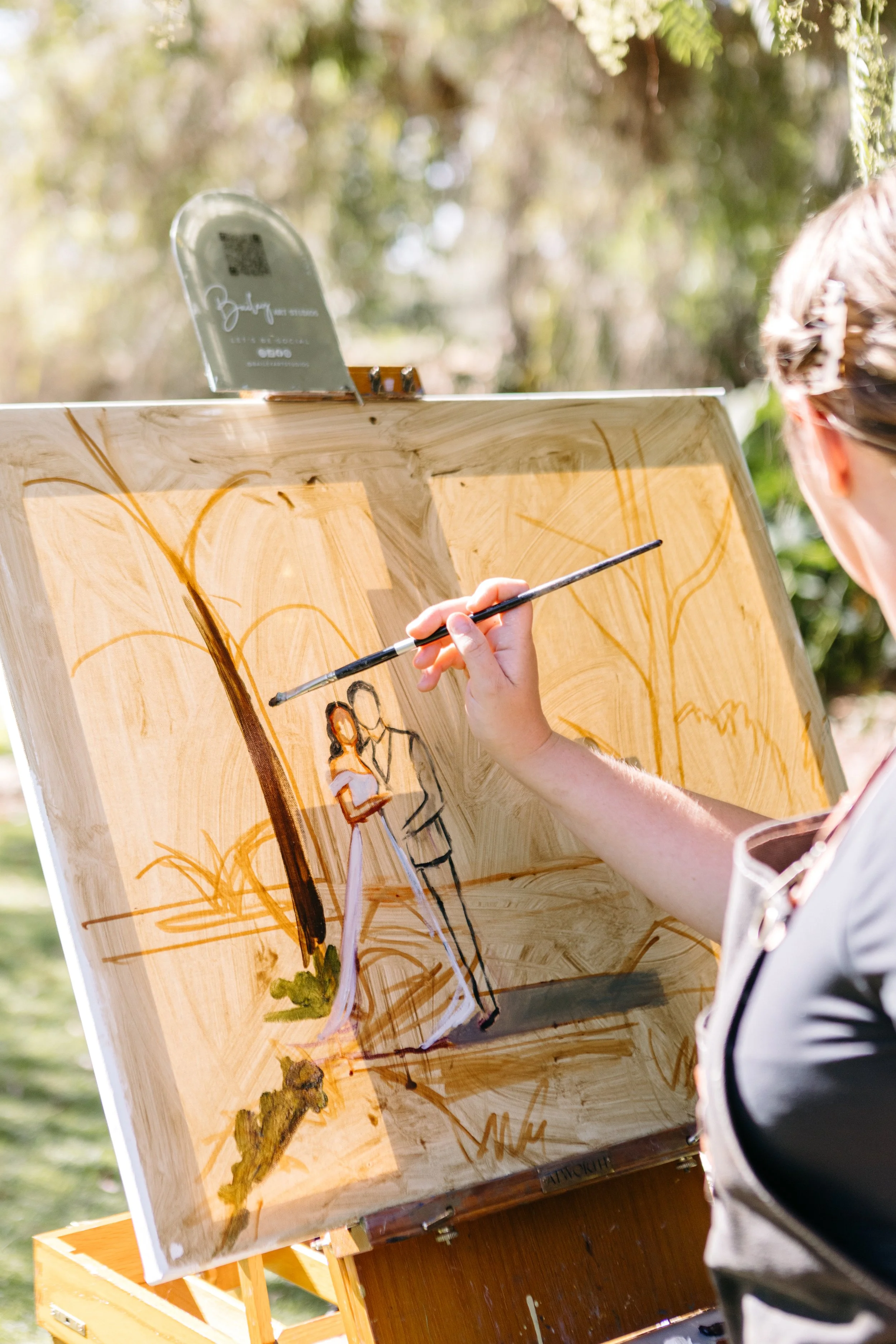 Person painting on a wooden canvas outdoors, with trees in the background.
