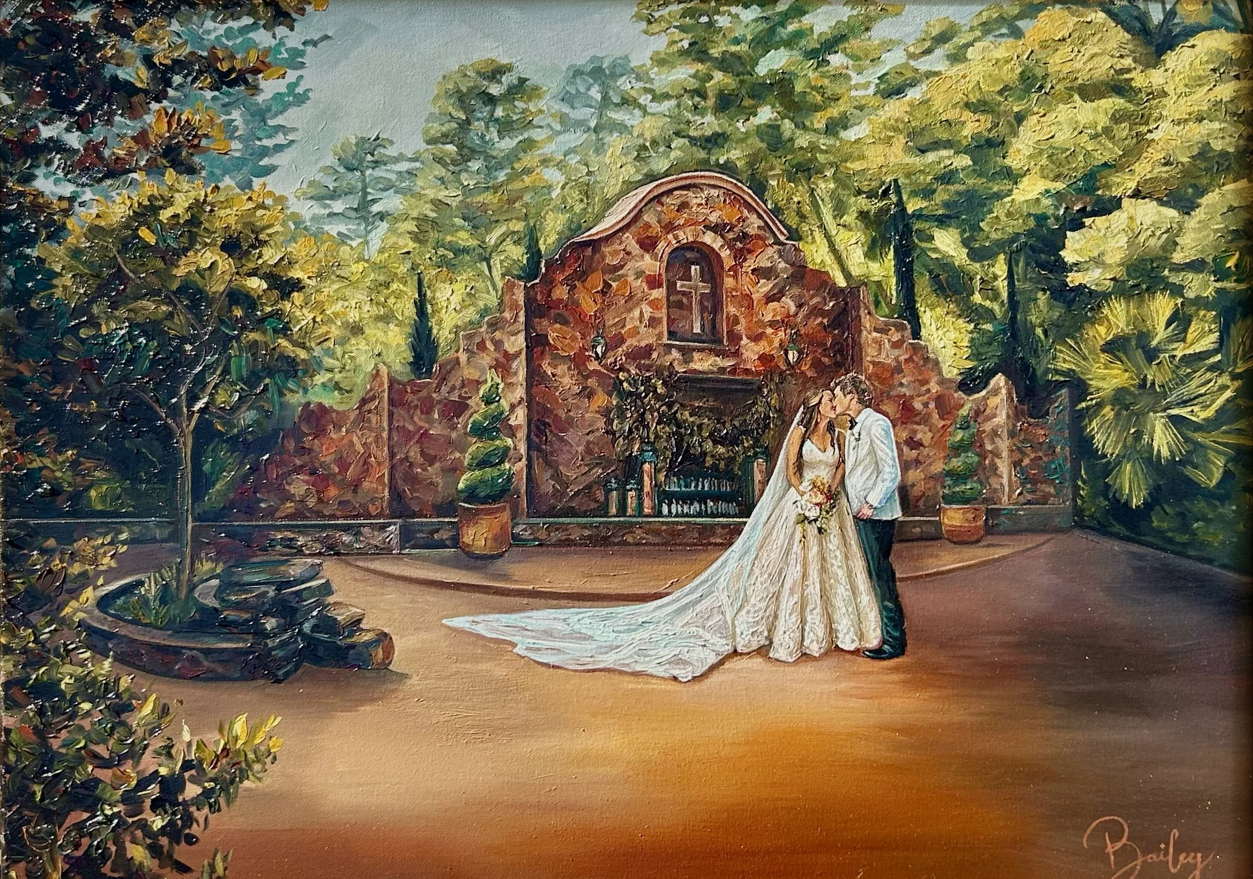 A bride and groom standing close together, sharing a kiss outdoors in front of a rustic stone chapel with a cross, surrounded by lush greenery and potted plants.
