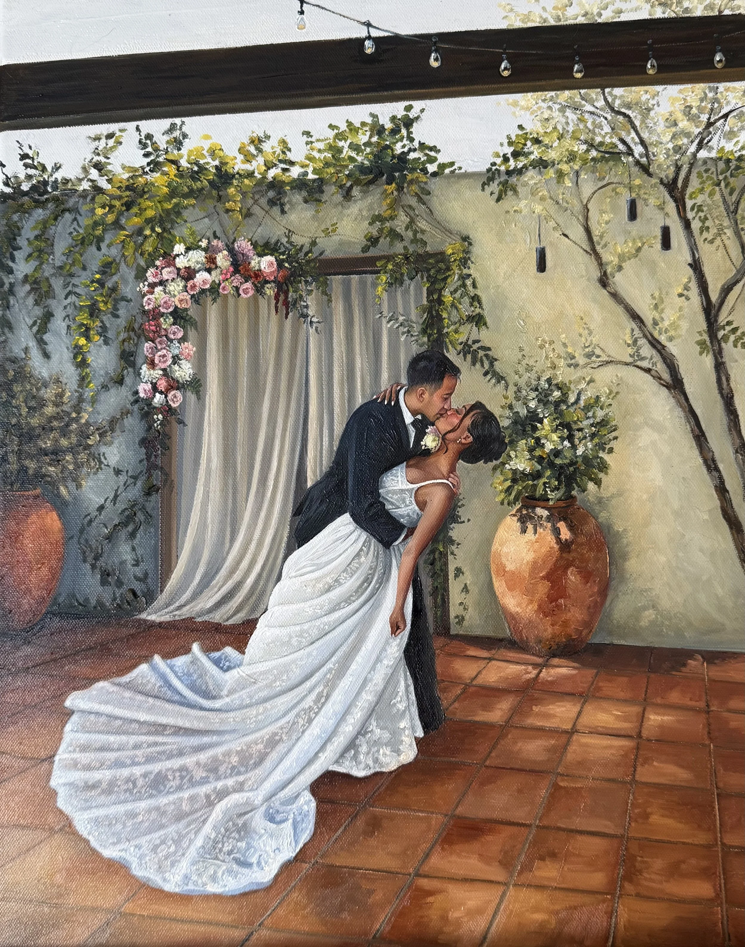 A newlywed couple dancing beneath a floral archway with draped white fabric. The groom in a black tuxedo and the bride in a white wedding dress are sharing a kiss. The background has green vine-covered walls, large potted plants, and hanging string l