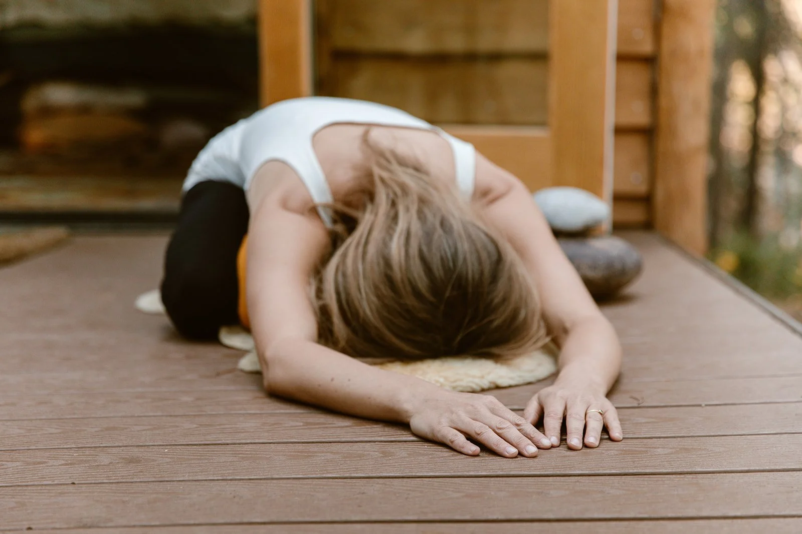 Woman practicing child's pose yoga on wooden deck.
