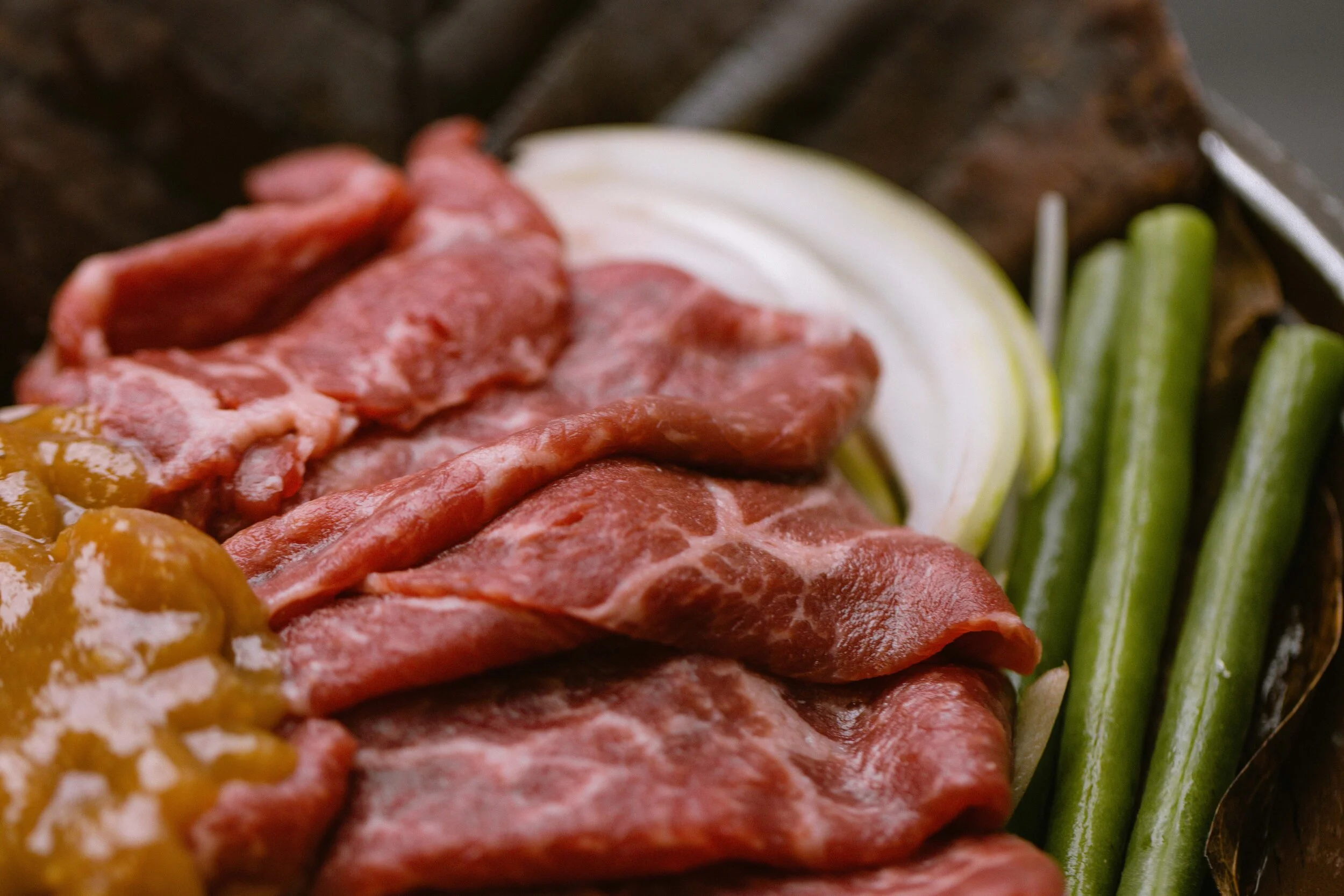 Wagyu Beef Hooba Yaki. Raw beef slices, sliced onions, and green beans arranged on a rustic surface. 奥克兰武藏日本料理餐厅. Musashi Japanese Restaurant, Auckland, St Heliers & Milford.