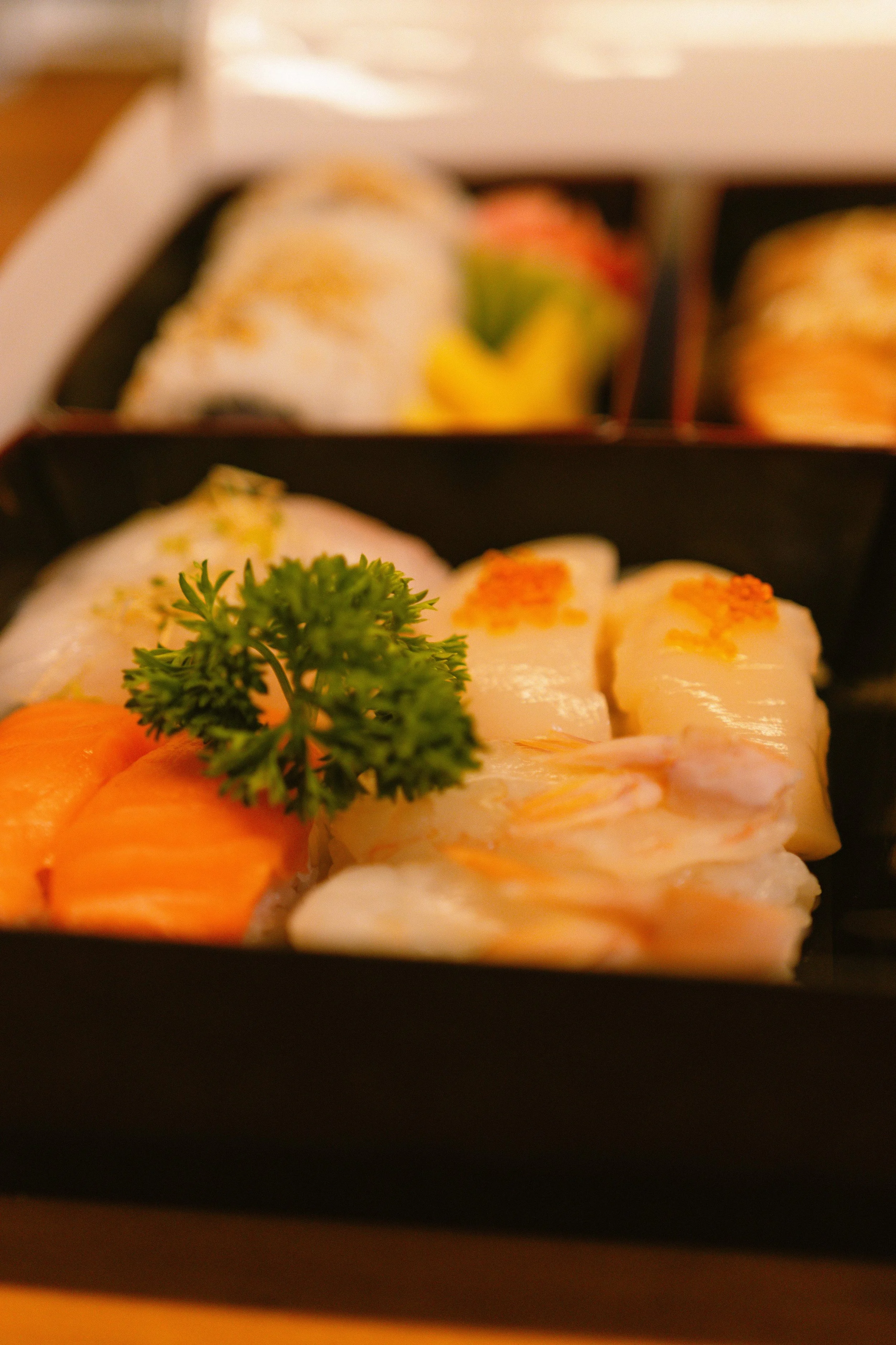 Close-up of assorted sushi pieces, garnished with parsley and fish roe, in a black bento box. 奥克兰武藏日本料理餐厅. Musashi Japanese Restaurant, Auckland, St Heliers & Milford.