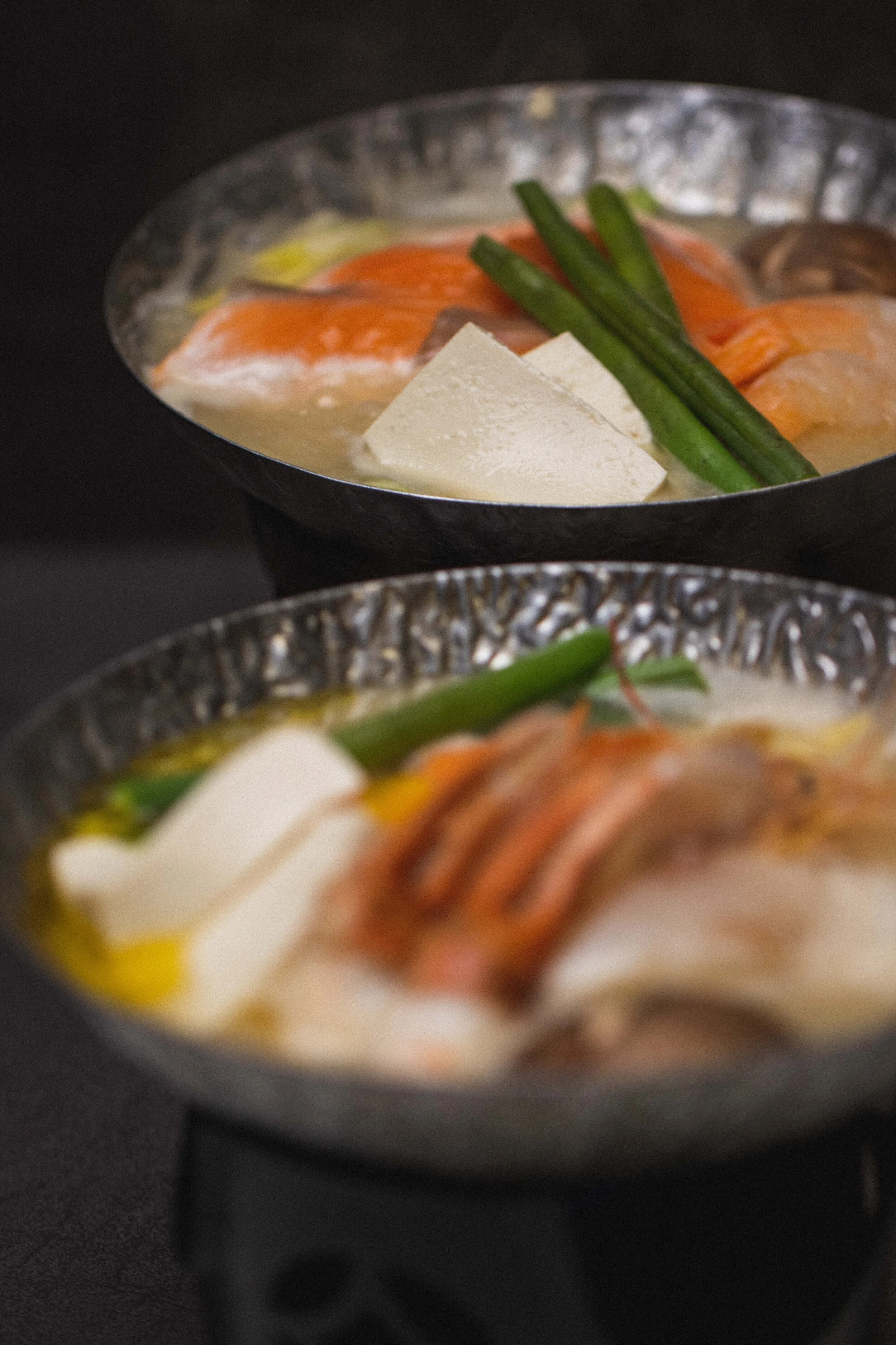 Two bowls of Japanese hot pot, possibly shabu-shabu or sukiyaki, with pieces of tofu, green onions, and slices of meat in broth. 奥克兰武藏日本料理餐厅. Musashi Japanese Restaurant, Auckland, St Heliers & Milford.