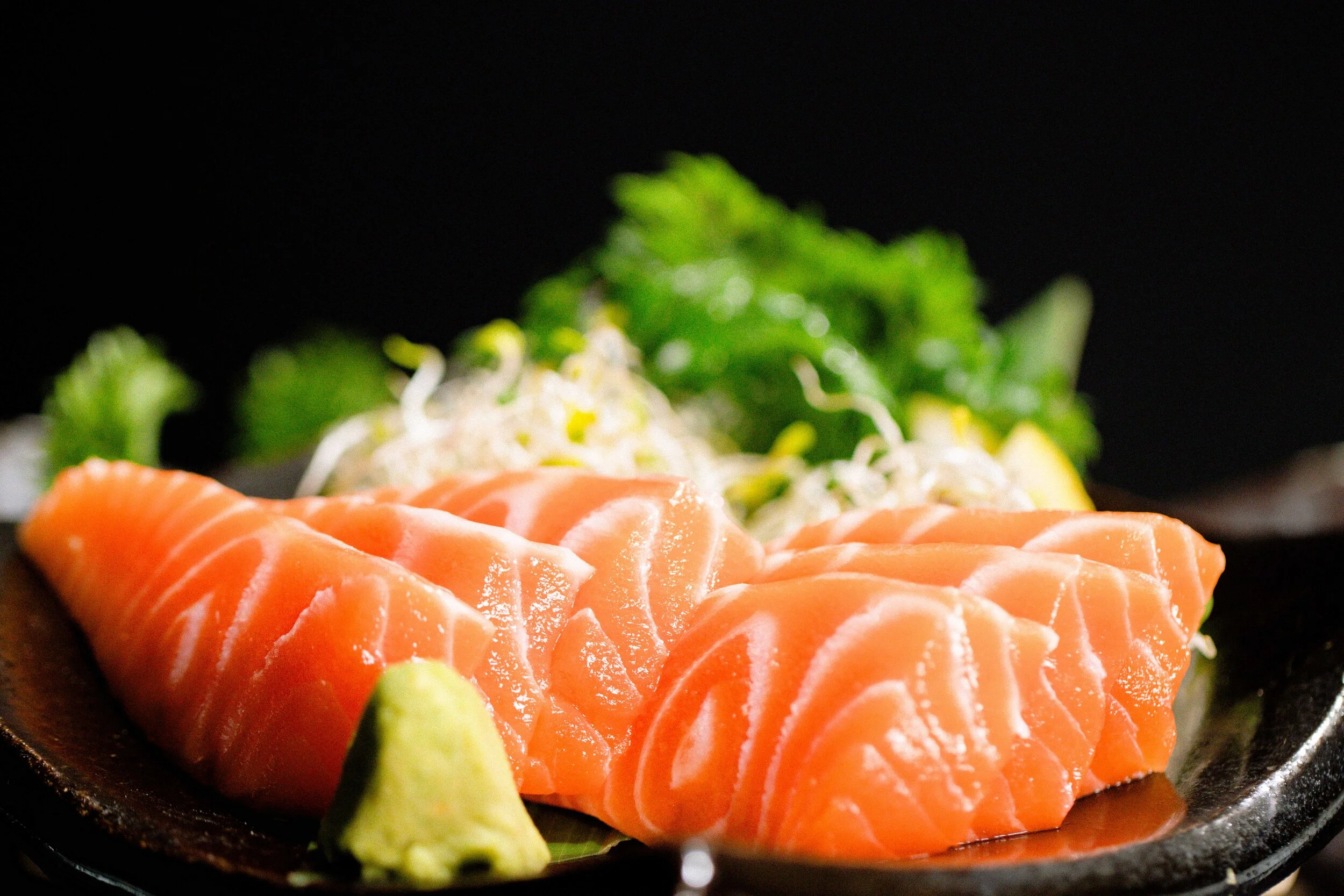 Slices of fresh salmon sashimi with wasabi and garnishes on a black plate. 奥克兰武藏日本料理餐厅.