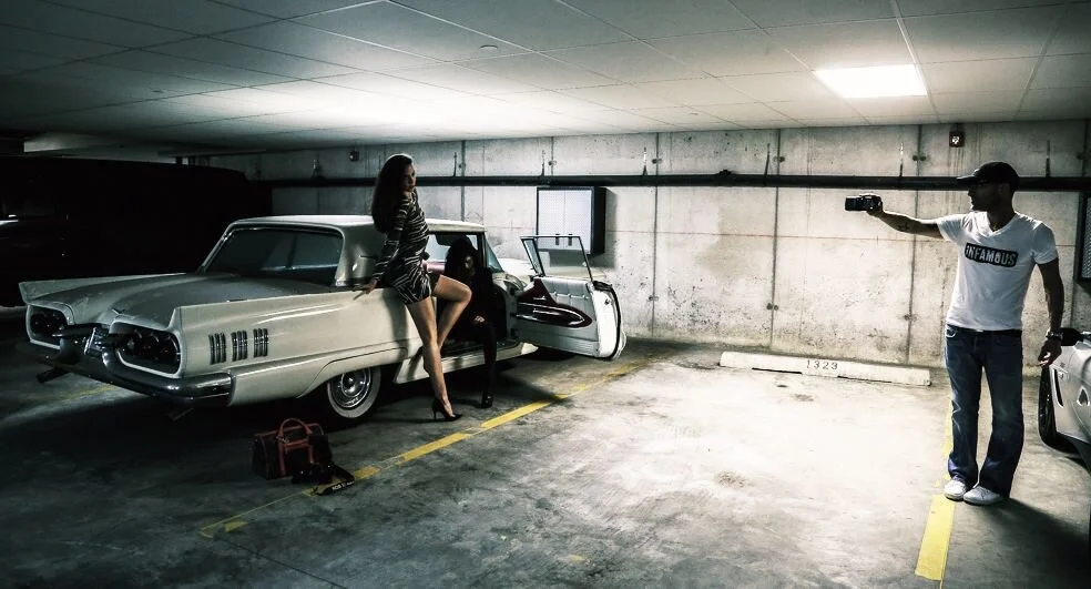 Woman in striped dress posing on vintage car in parking garage, man recording with camera