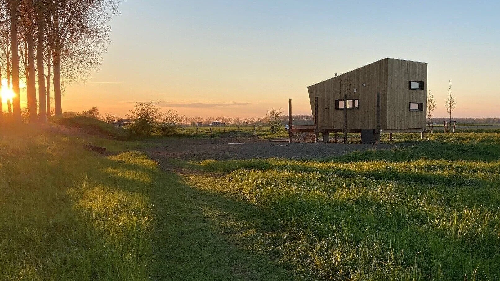 Tiny House in Zeeland op palen bij De Dijck , met de zon ondergaande op de achtergrond