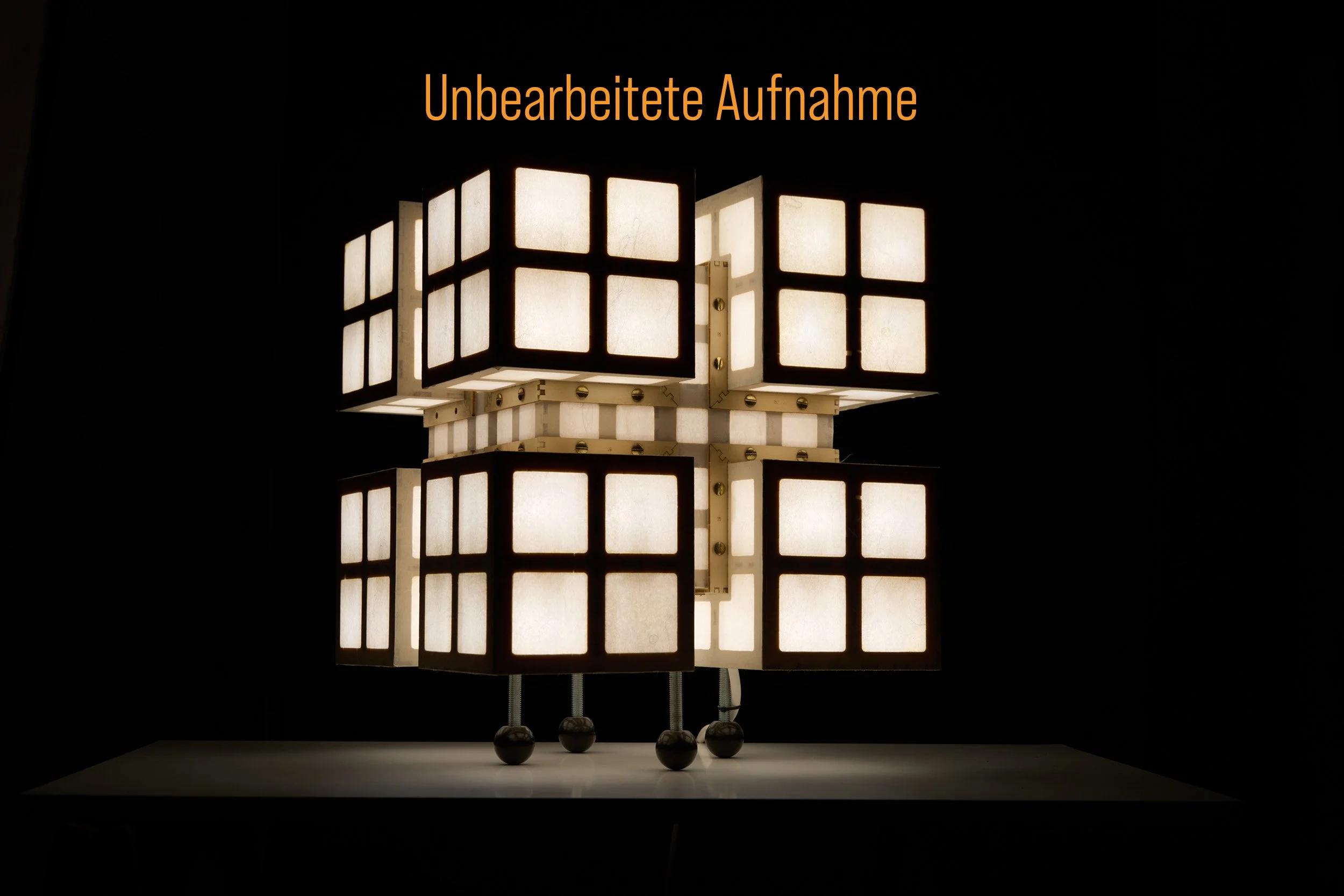 Ein ungewöhnlicher, mehrstöckiger Lampenschirm mit quadratischen Abschnitten, beleuchtet vor einem schwarzen Hintergrund, mit dem deutschen Text "Unbearbeitete Aufnahme" oben