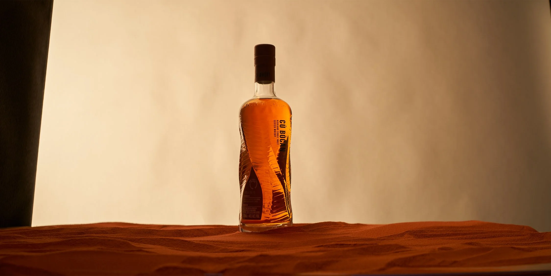 Eine Flasche mit einer hellbraunen Flüssigkeit steht auf einem Holztablett vor einem hellen Hintergrund.