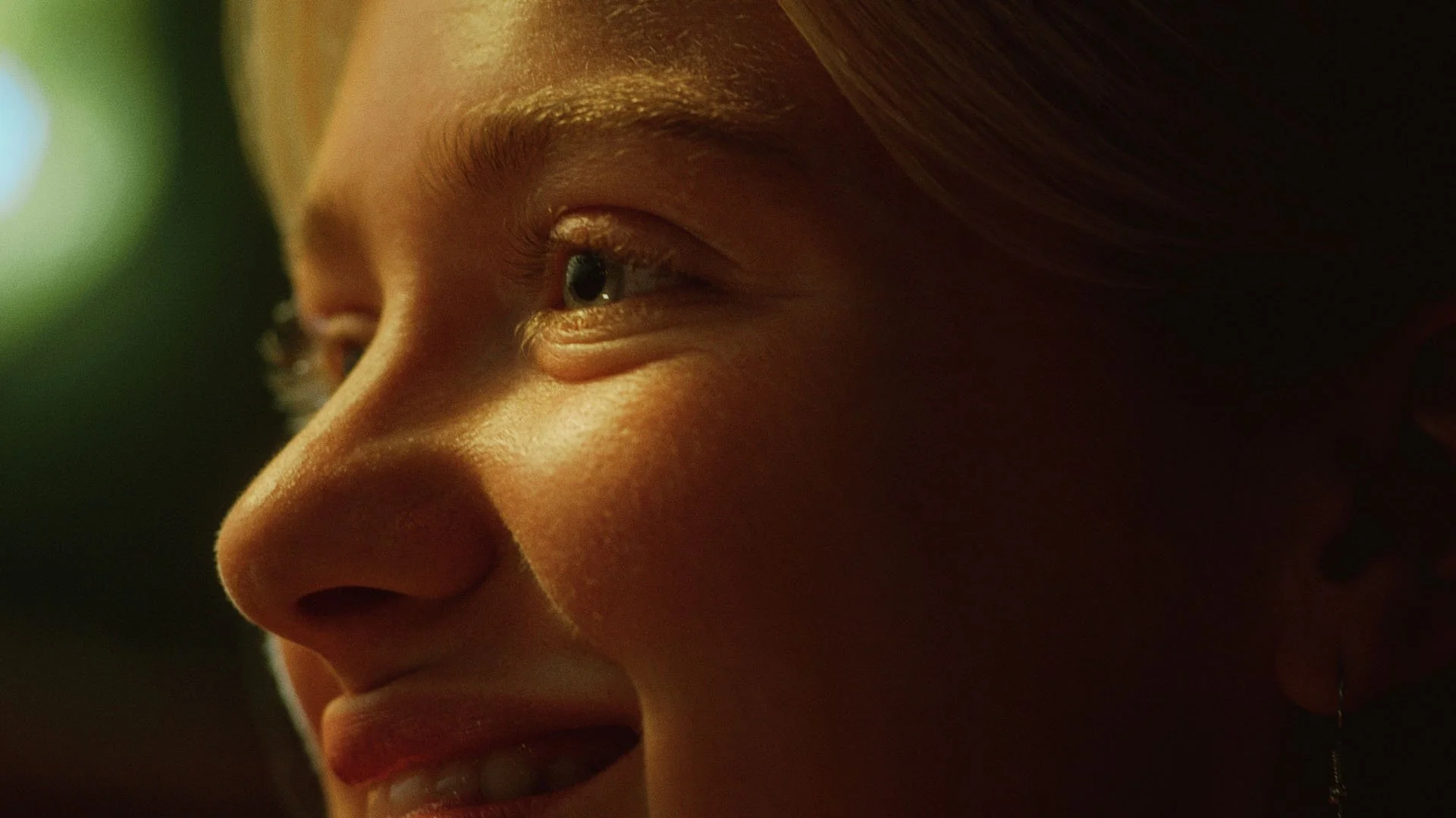 Nahaufnahme eines lachenden jungen Mädchens, das nach rechts schaut, mit Lichtreflexen im Gesicht und einem grünen Hintergrund.