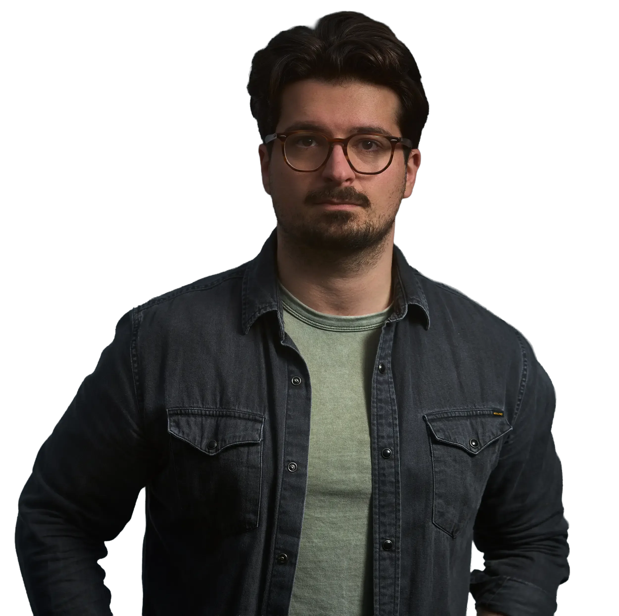 Porträt eines Mannes mit dunklen Haaren, Brille und Bart, trägt eine grüne T-Shirt und eine dunkle Jeansjacke, vor dunklem Hintergrund.