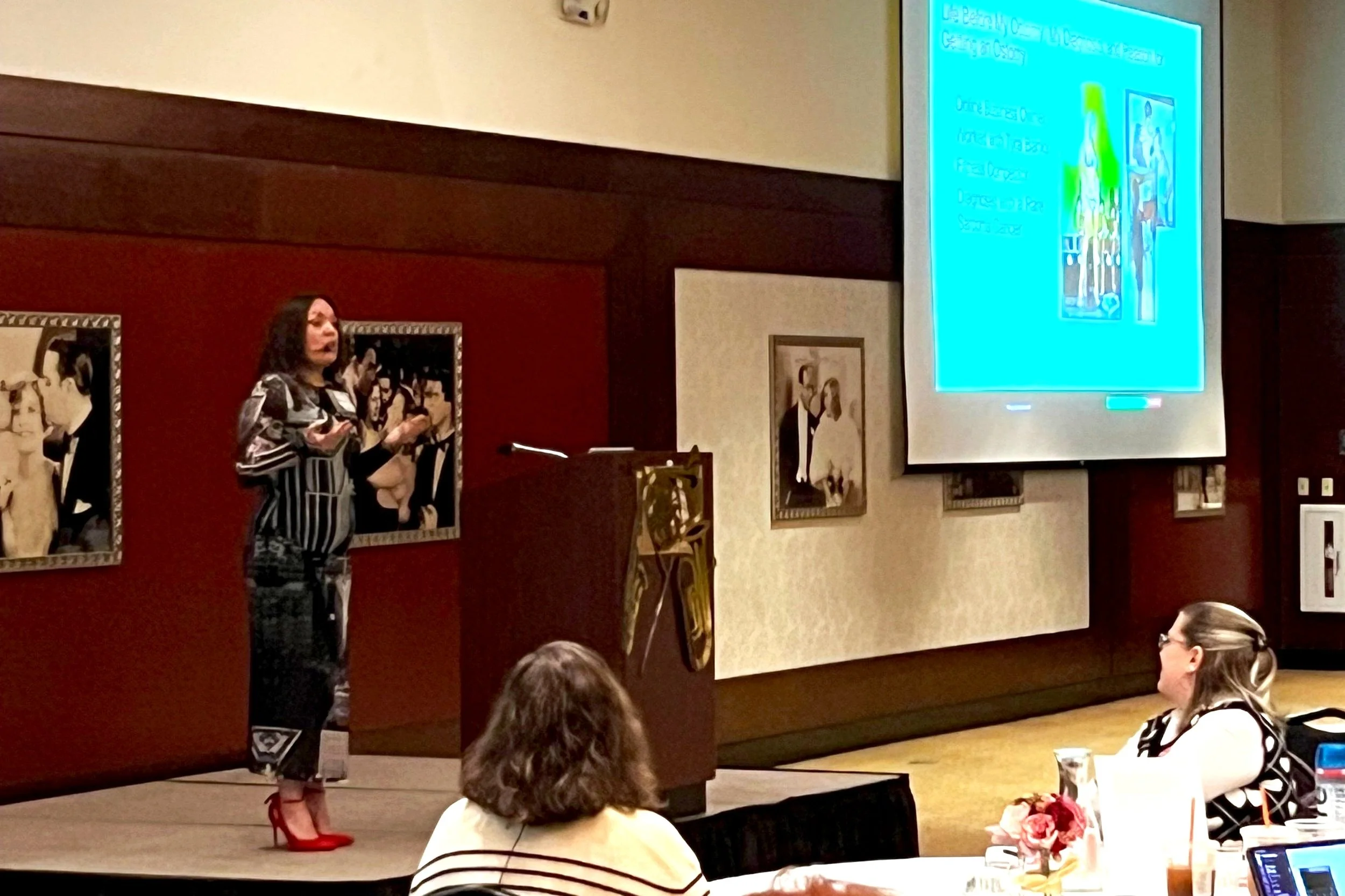 A woman in a patterned dress and red high heels is giving a presentation at a conference, standing next to a large screen displaying a slide about Google Ads.