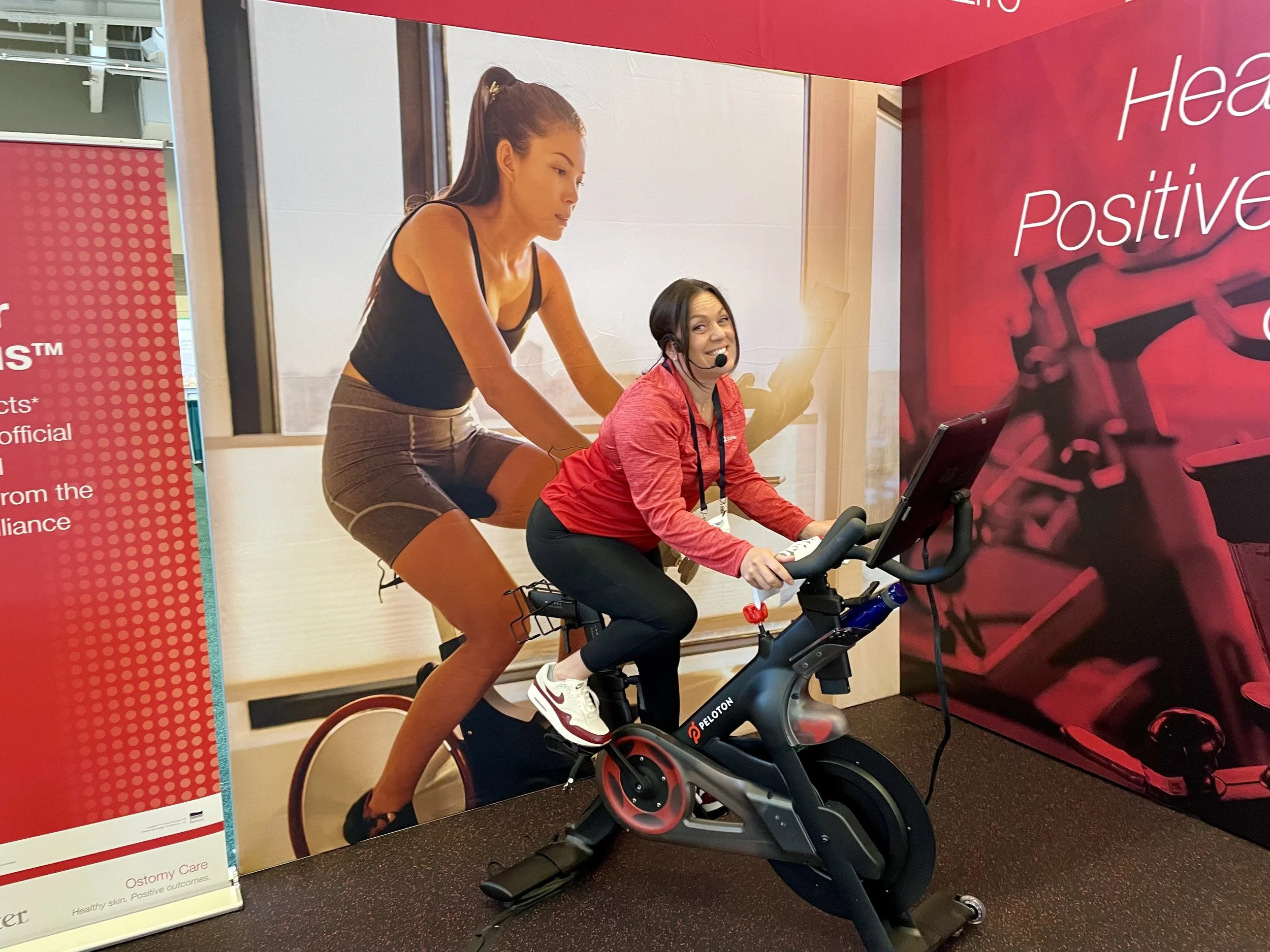Woman smiling while riding a stationary exercise bike with a large poster of a person working out behind her.