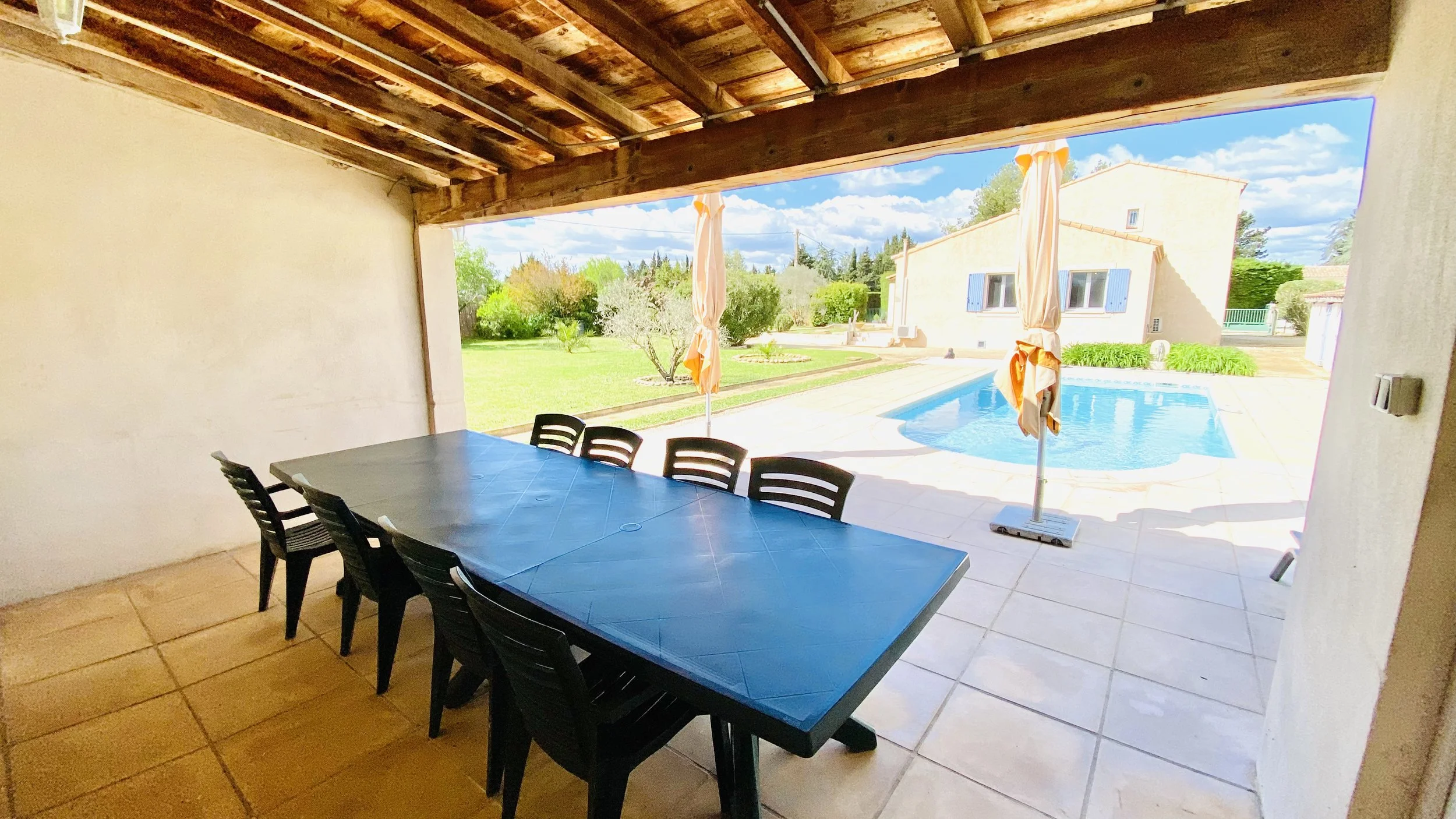 Covered terrace dining space overlooking the swimming pool and garden of a Mediterranean villa