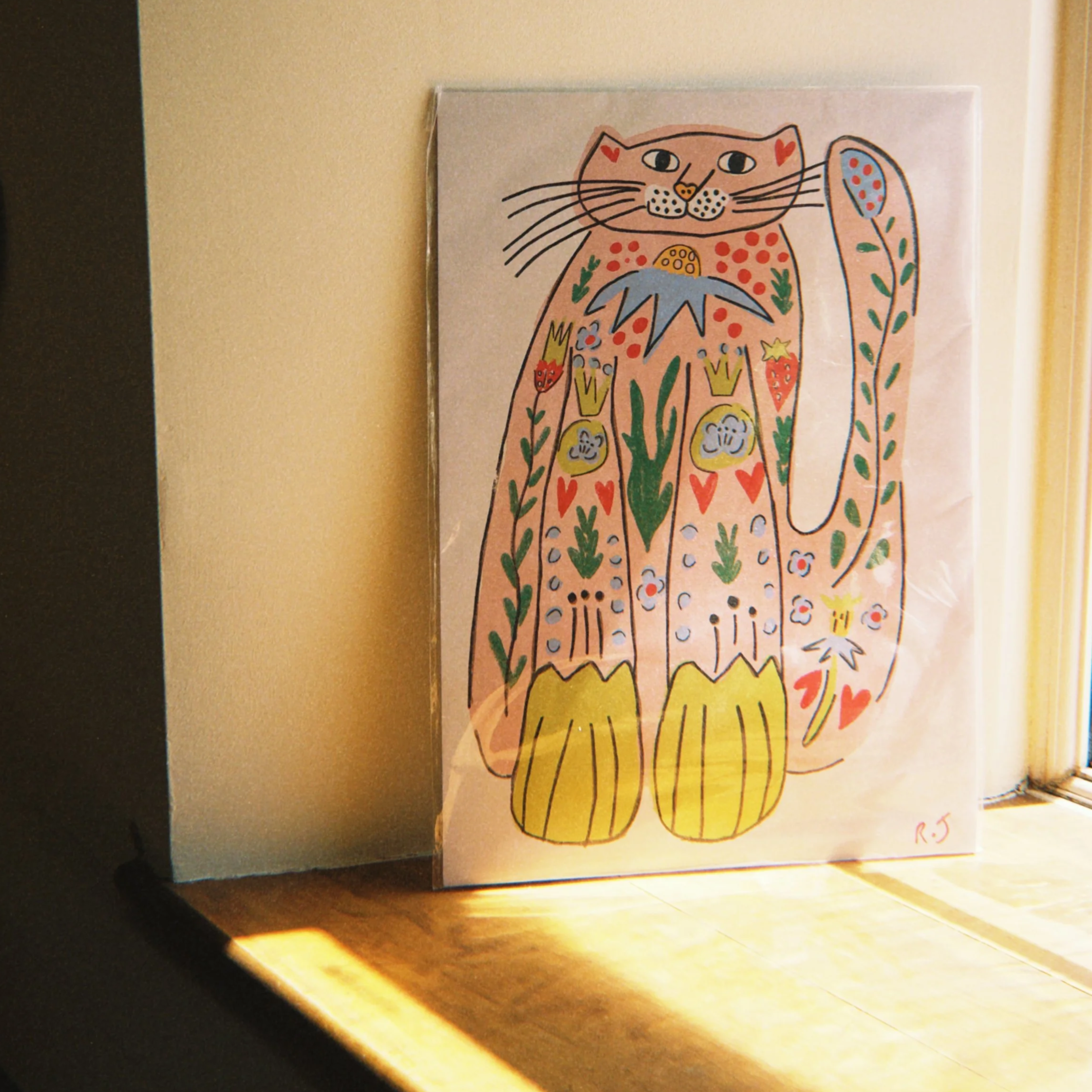 Colorful drawing of a cat with decorated body and a large fish at its side, mounted on a beige wall.