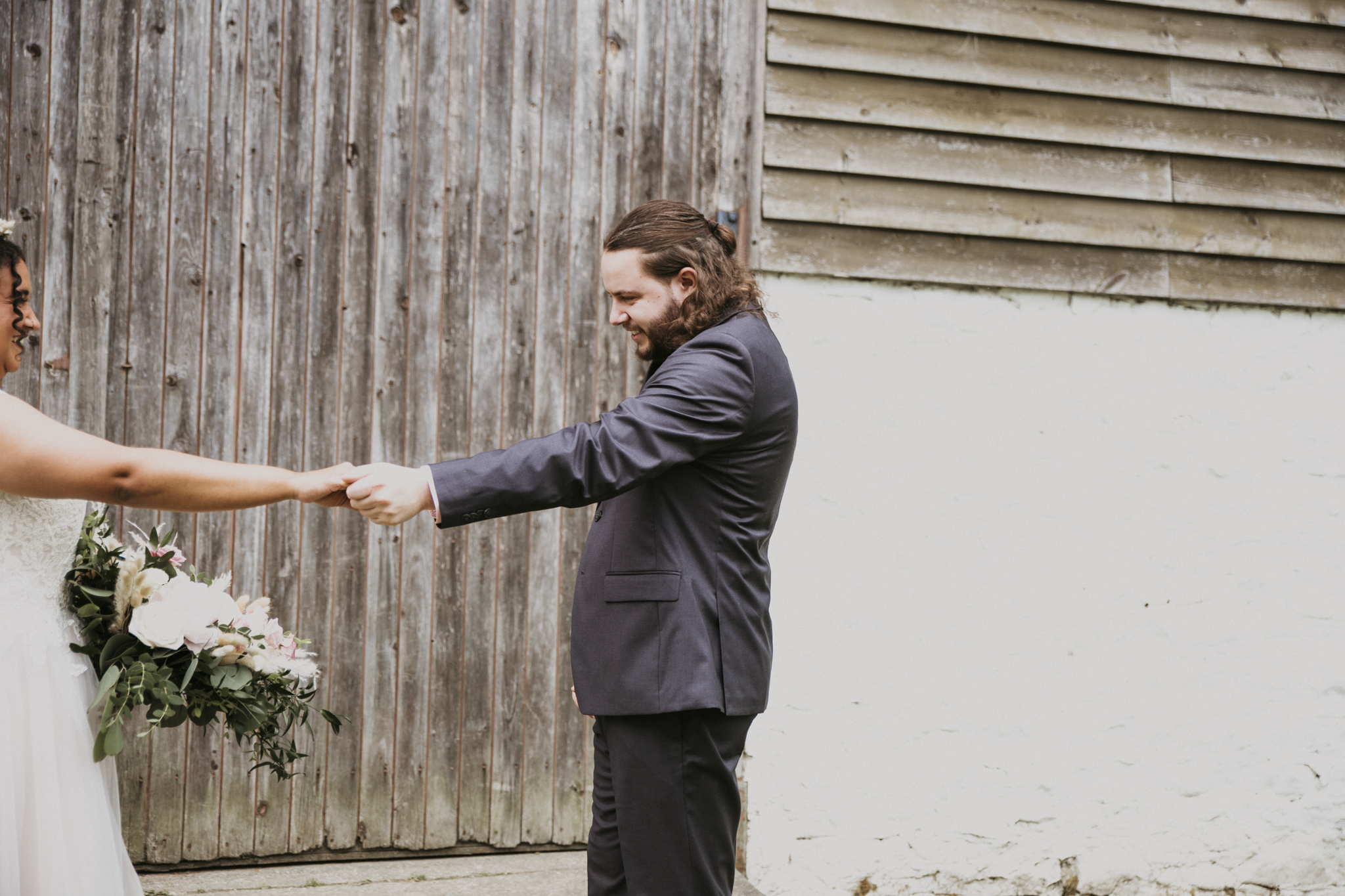 A man in a gray suit holding hands with a woman in a white dress holding a bouquet of flowers during a wedding.