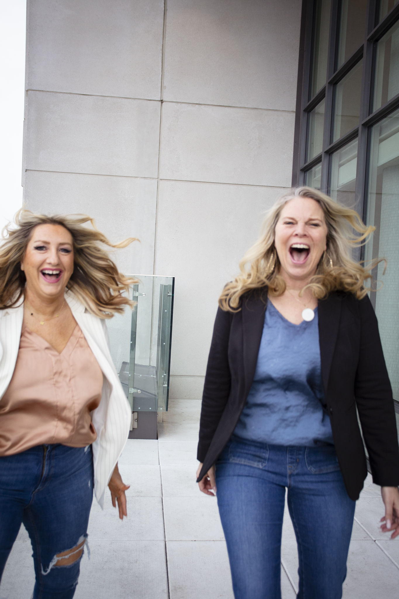 Two women smiling and laughing outdoors on a modern building balcony or terrace.