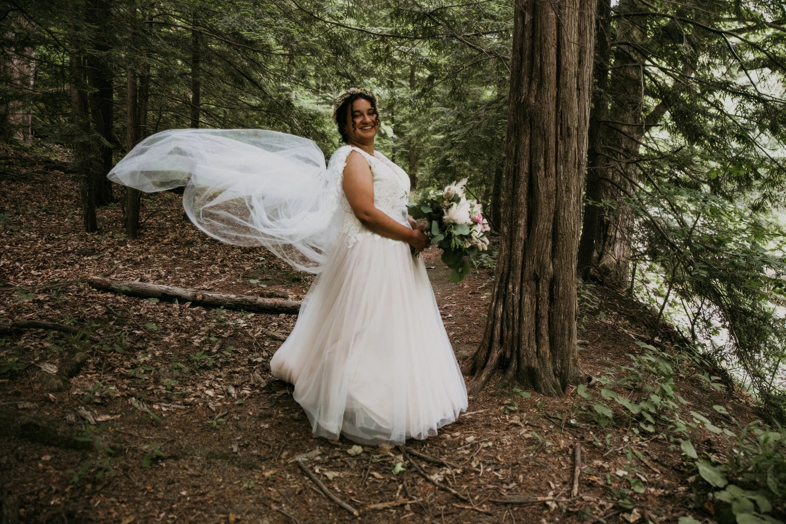 Bride in a white wedding dress holding a bouquet of flowers standing in a forest.