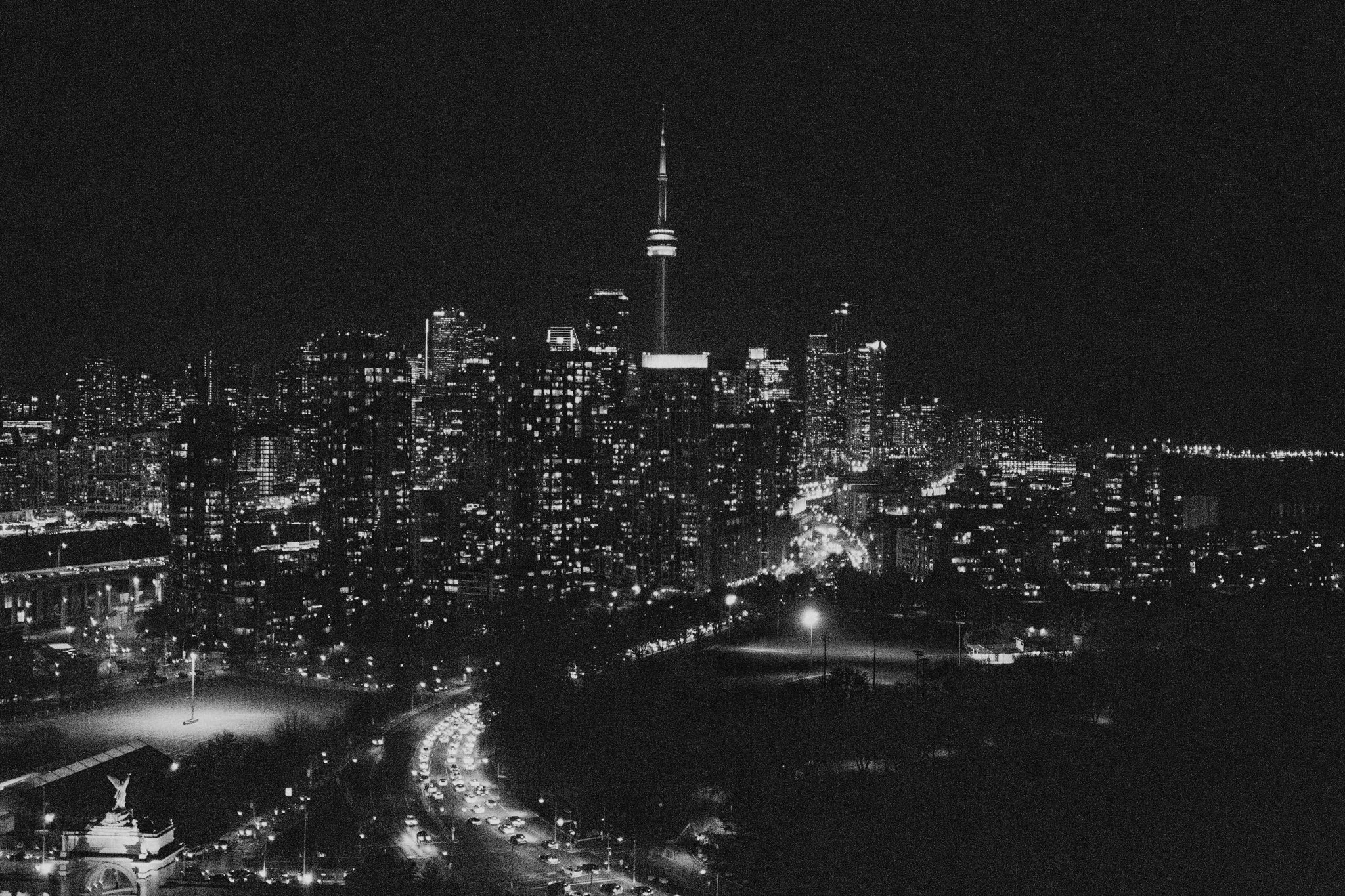 Nighttime view of Toronto city skyline with the tall lit CN Tower and buildings, and a busy, curving road with traffic.