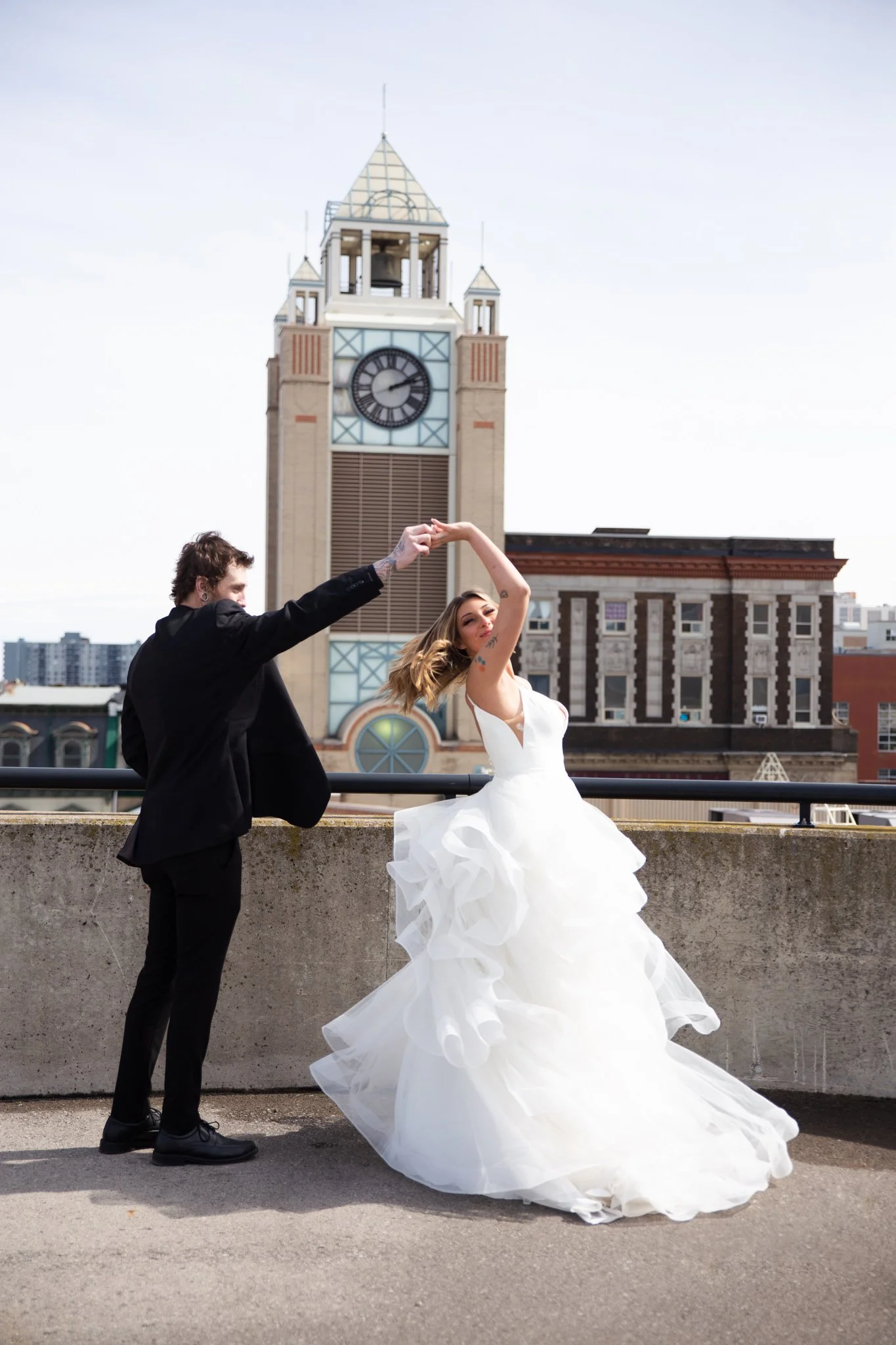 A bride and groom dancing on a rooftop with a clock tower and city buildings in the background.