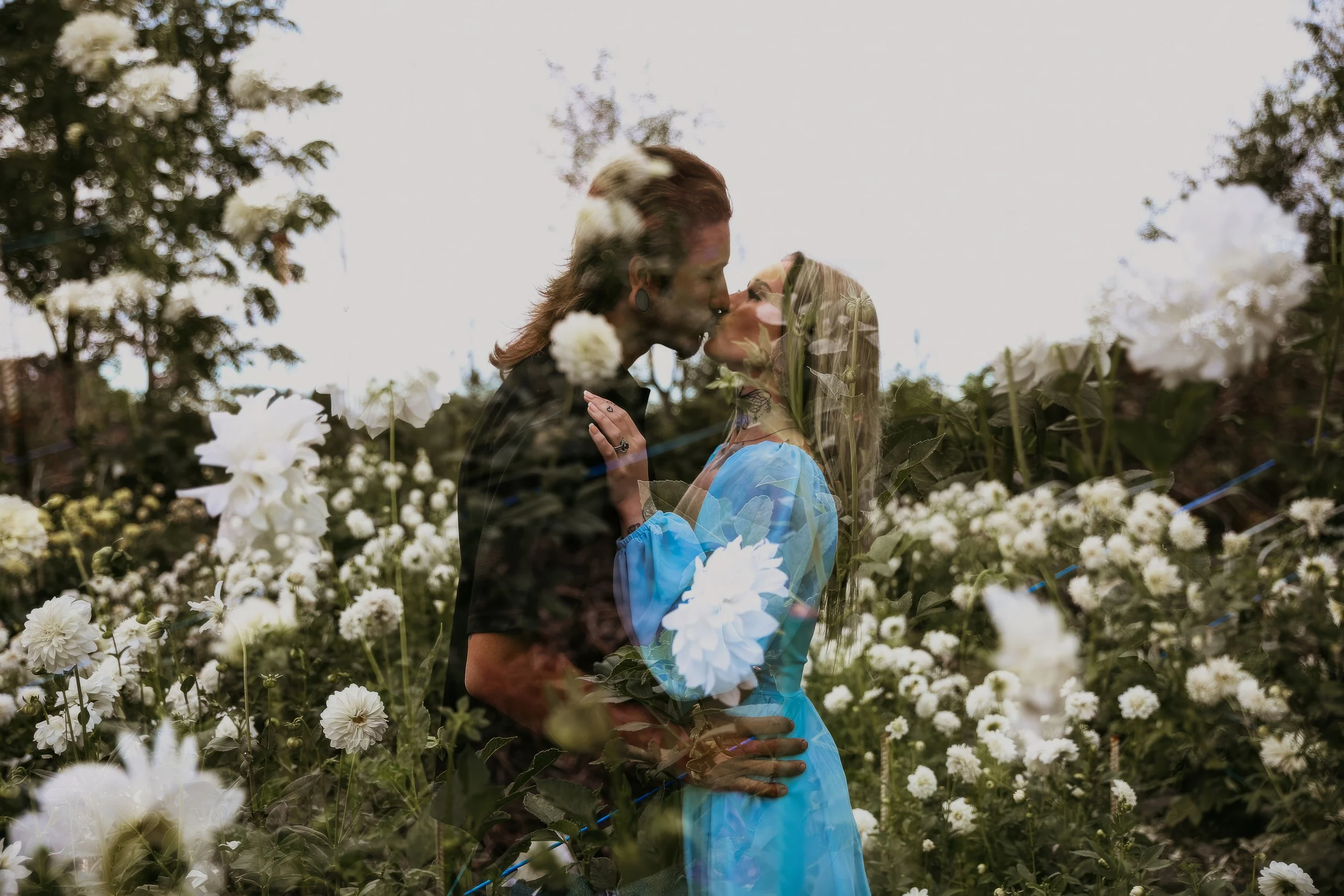 A couple kissing in a garden with white flowers, with a double exposure effect creating a layered appearance.