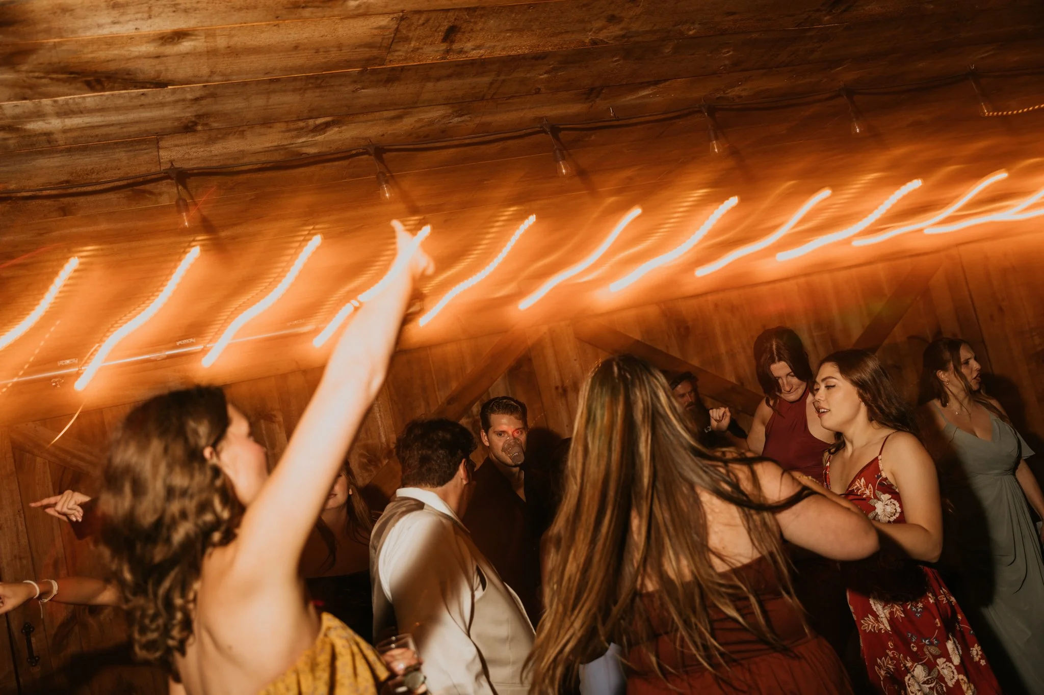 People dancing and socializing at a party with warm lighting and a rustic wooden ceiling.