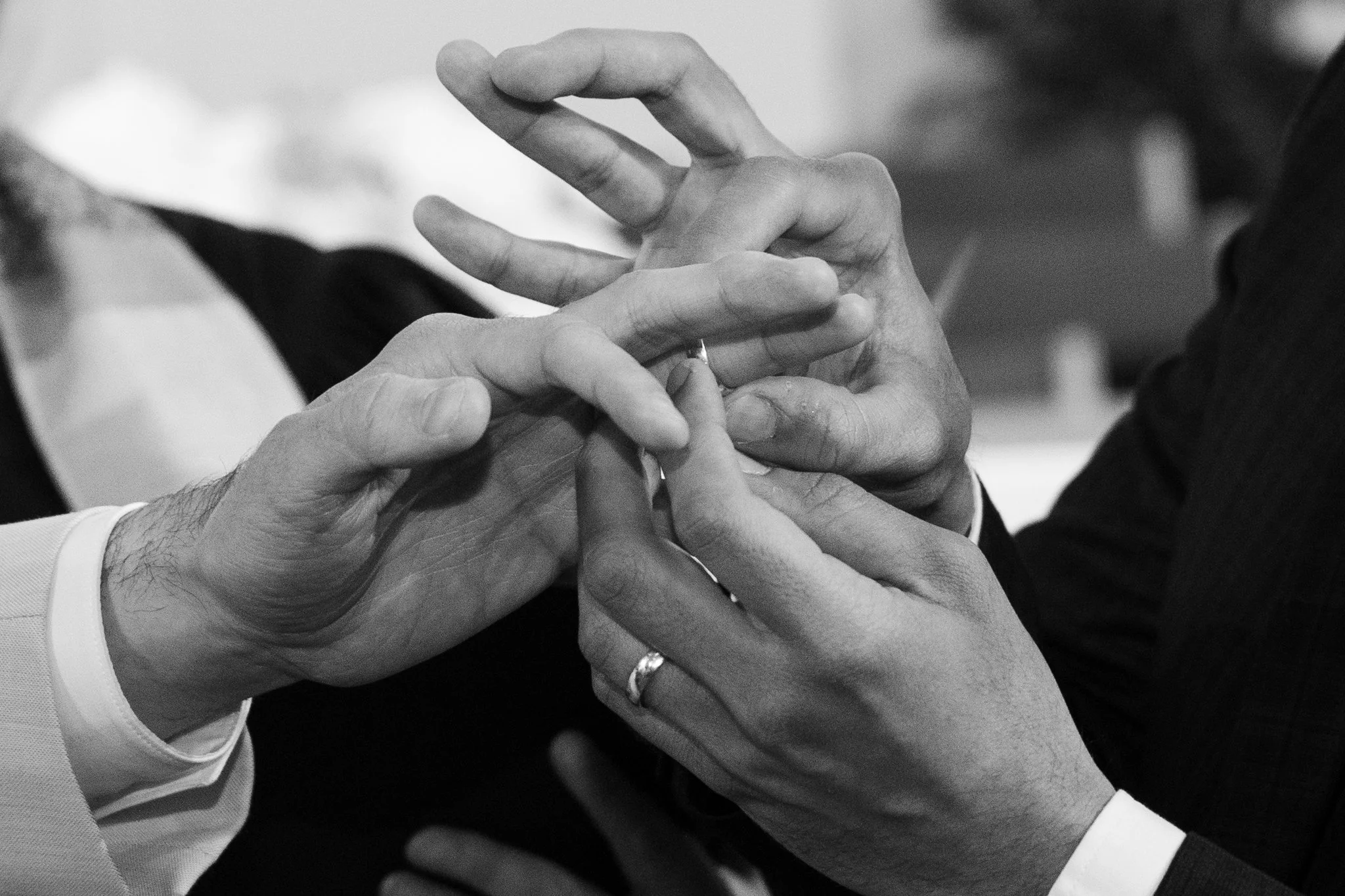 Two pairs of hands, one person is placing a ring on the other's finger during a wedding or engagement ceremony.