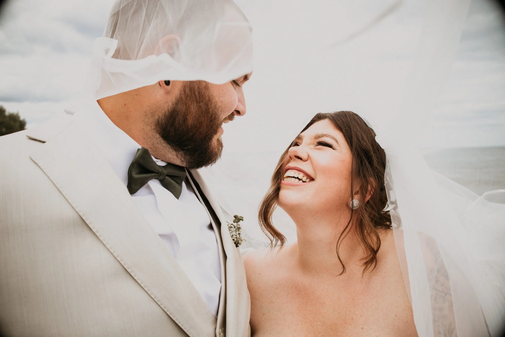 A bride and groom smiling and looking at each other outdoors on their wedding day.