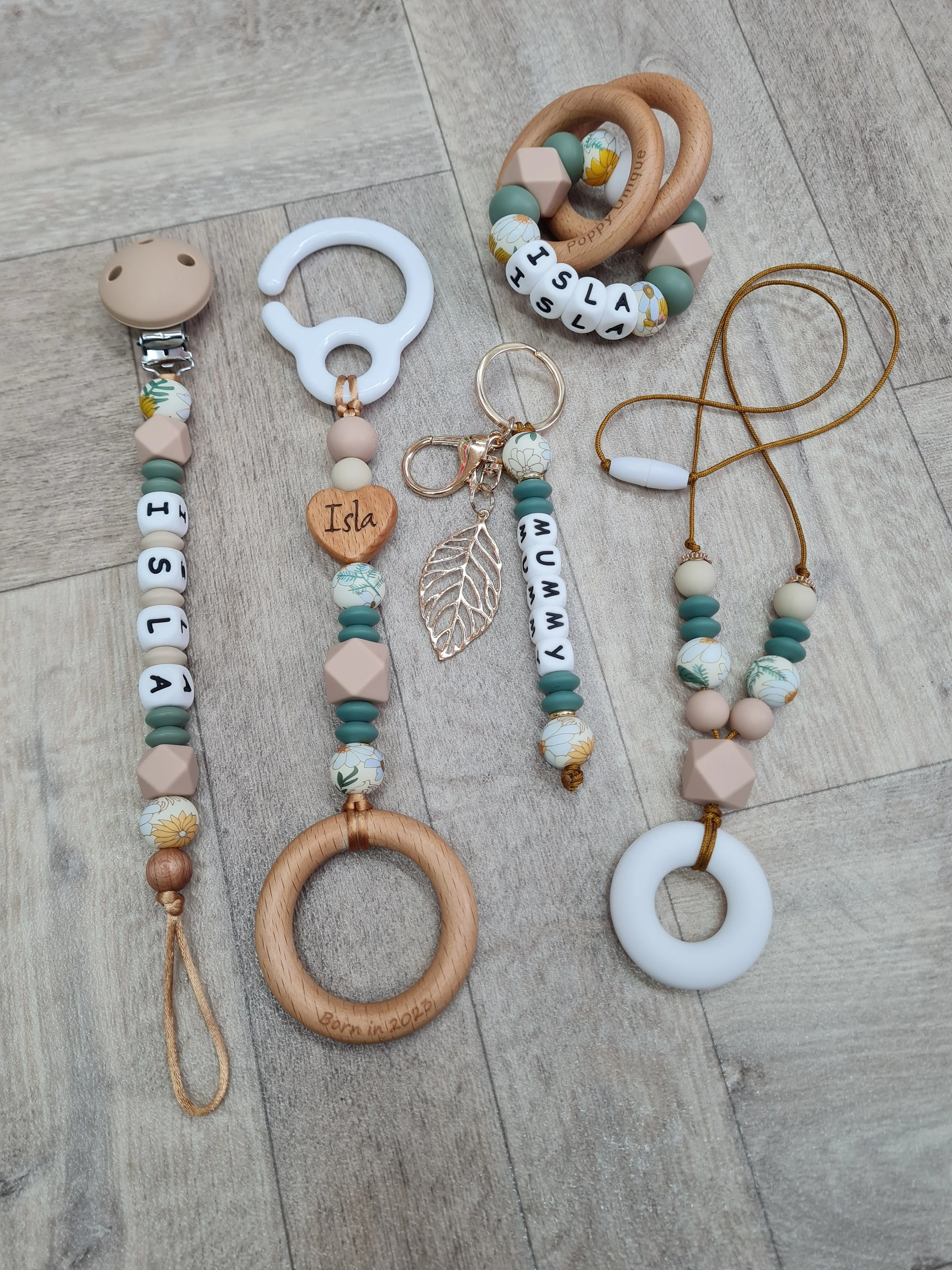 Baby accessories including pacifier clips, teething rings, bracelets with personalized beads spelling names on a wooden surface.