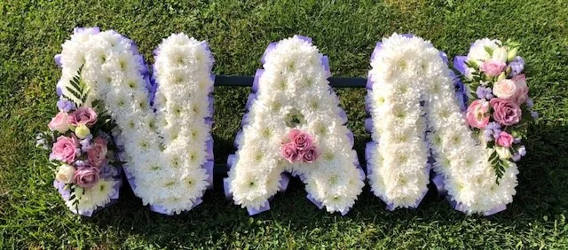 Flower arrangement spelling out the name 'NADIA' with pink and white flowers on a grassy background.
