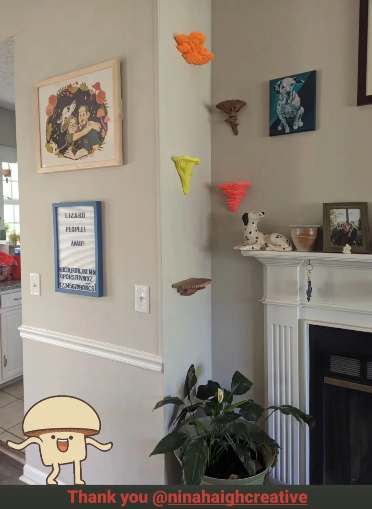 Decorative corner of a living room with artwork, shelves, and plants, including framed photos, animal figurines, colorful wall sculptures, and a cartoon mushroom character sticker.