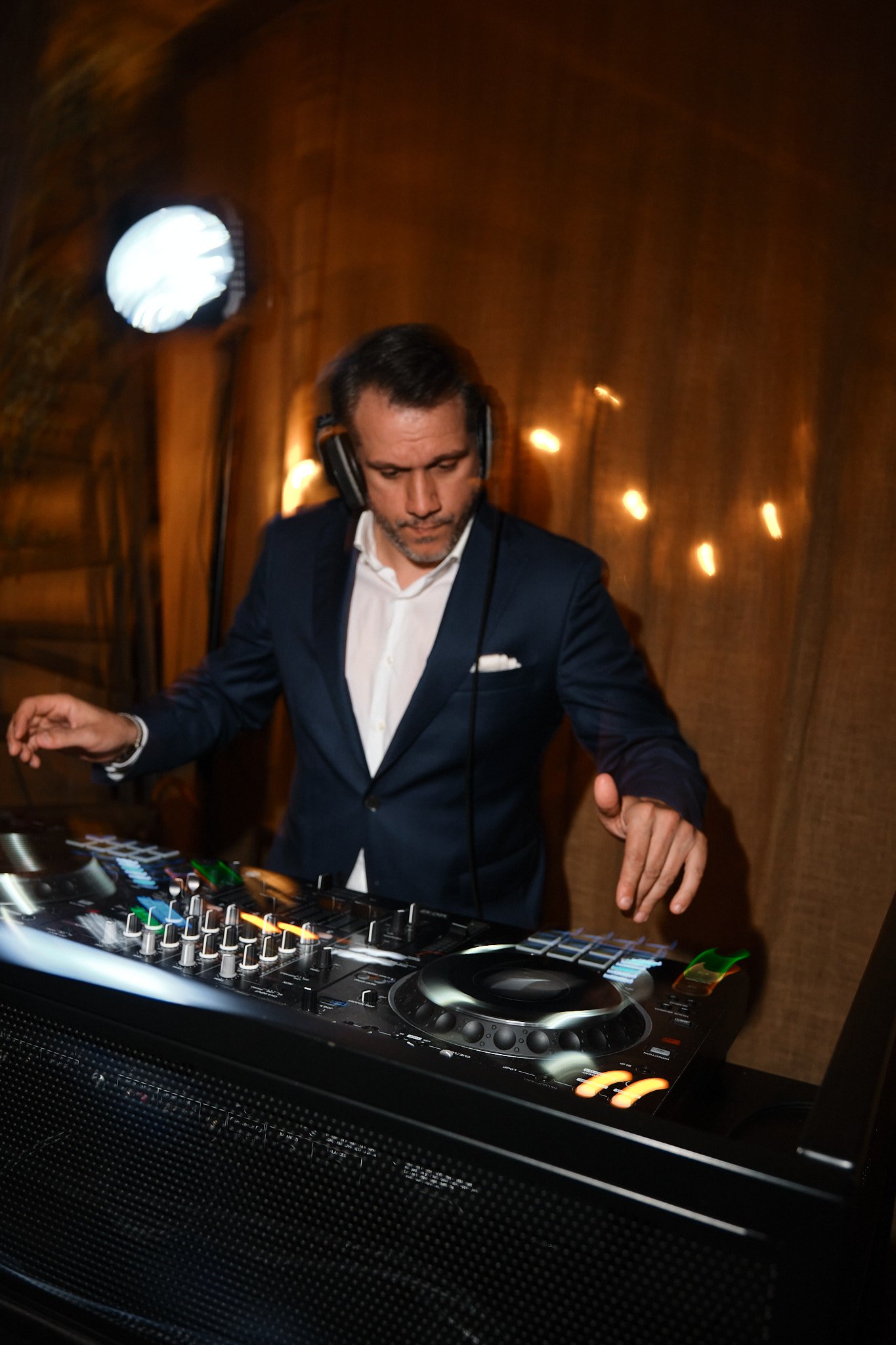 Man i formellt blå kostym som spelar musik på DJ-uppsättning i inomhusmiljö.