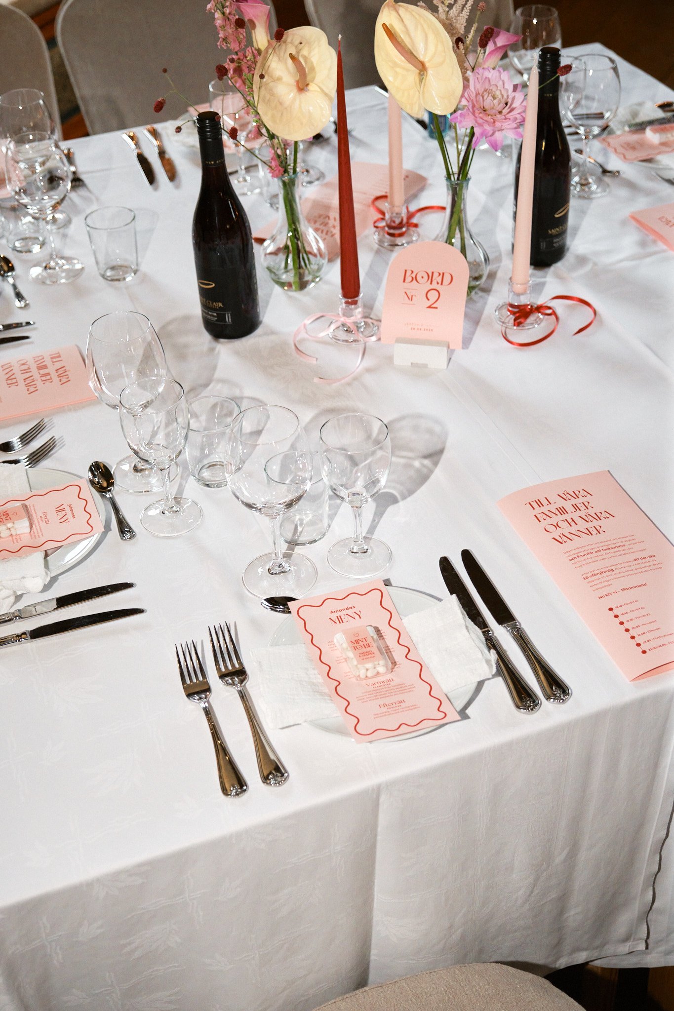 Elegant middagsdukning med tallrikar, bestick, dricksglas, blommor i vaser, lysande ljus, vinflaskor, och pinkfärgade menyer och bordsskyltar.