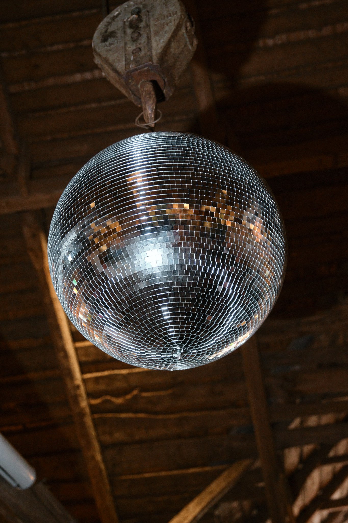 Disco boll av små speglar hängande i ett träbjälklag.