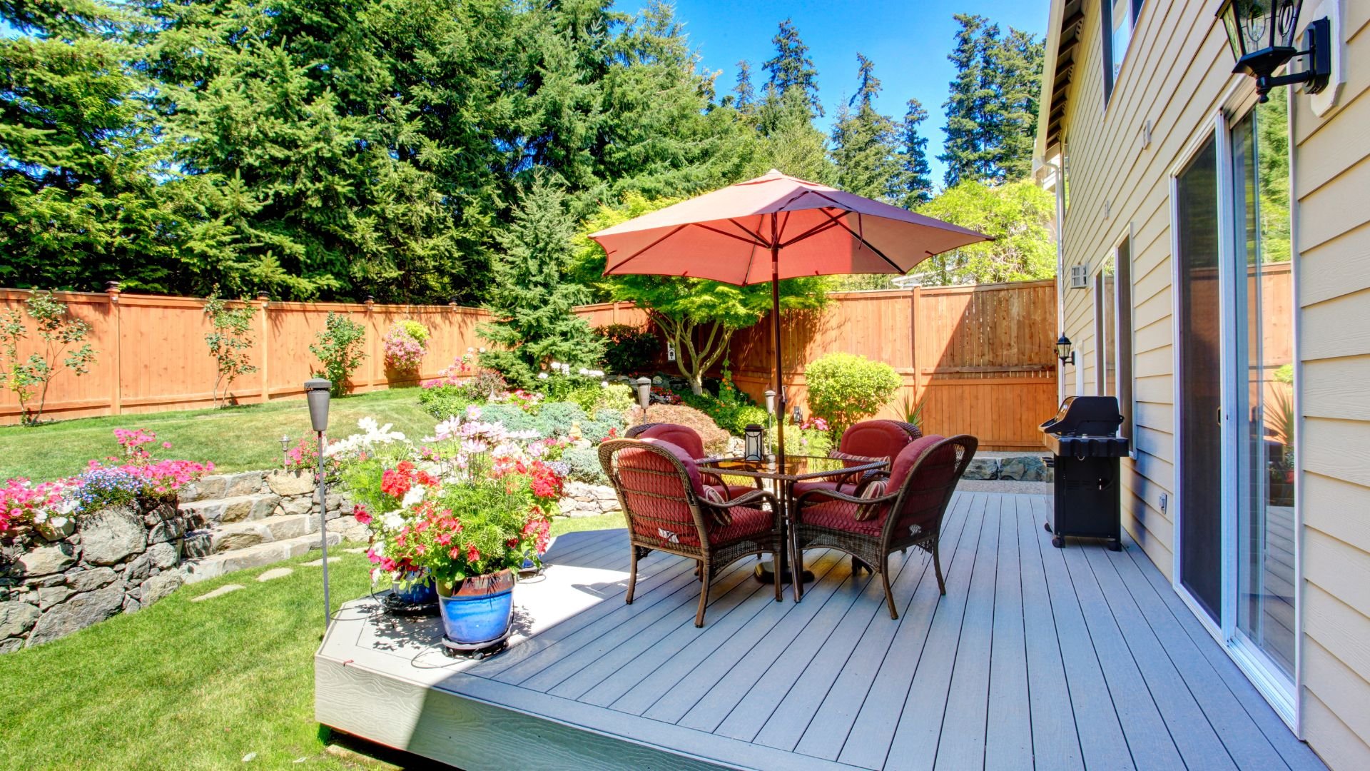 orange patio chairs and umbrella set on grey wood plank patio in backyard