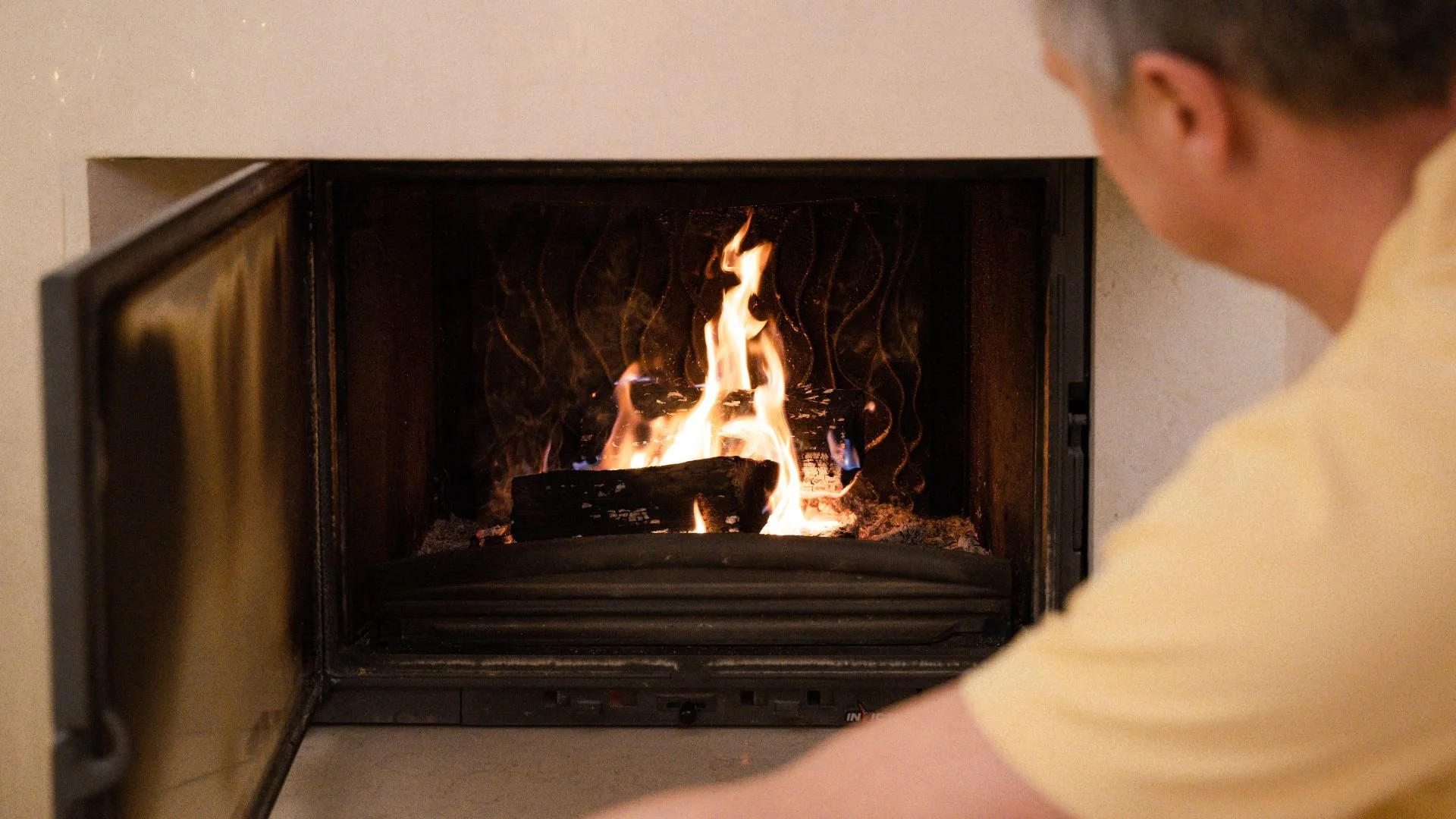 person opening firebox in side of wall with lit flame