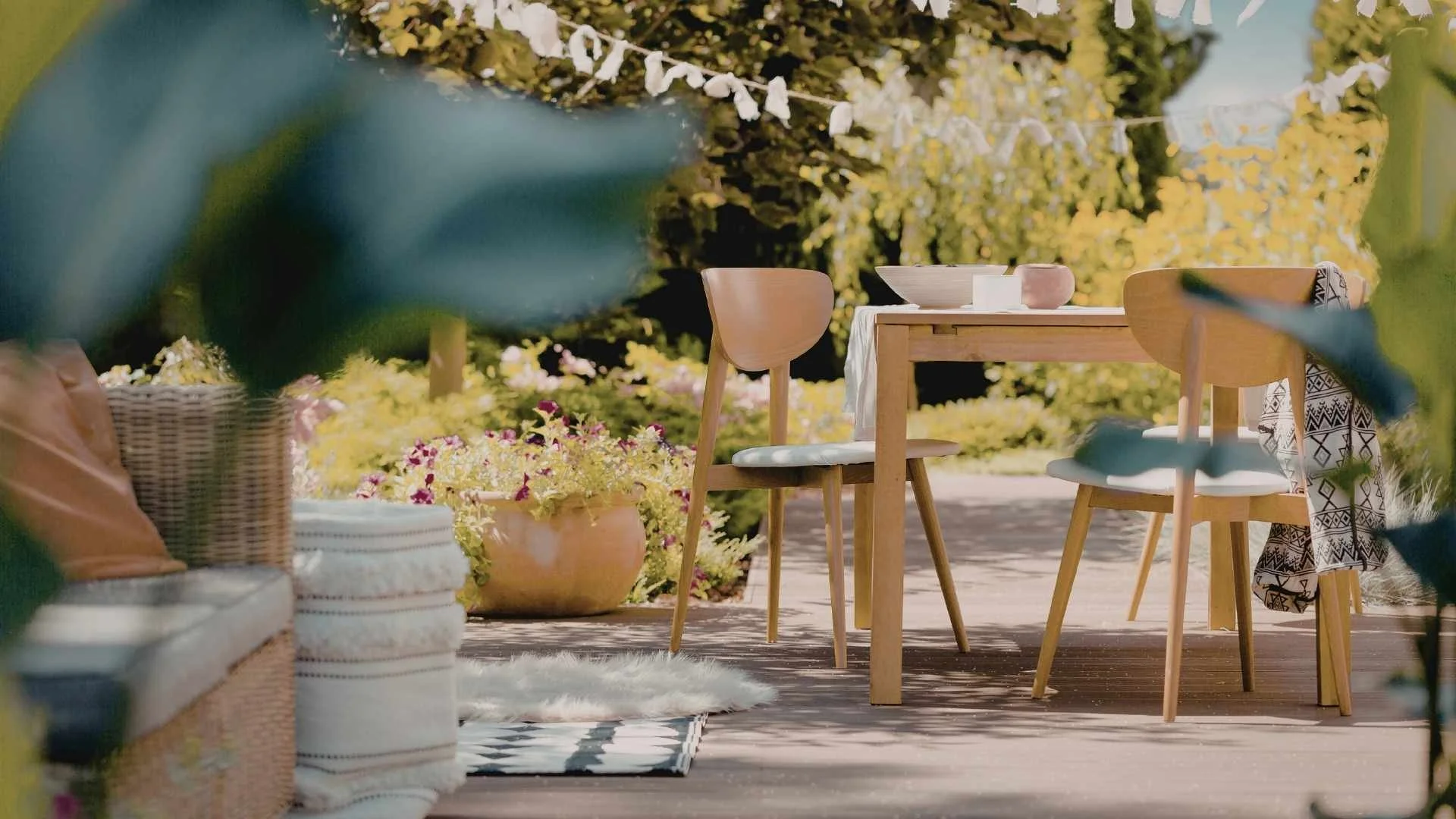 outdoor concrete patio with wooden chairs and table surrounded by various types of greenery and plants